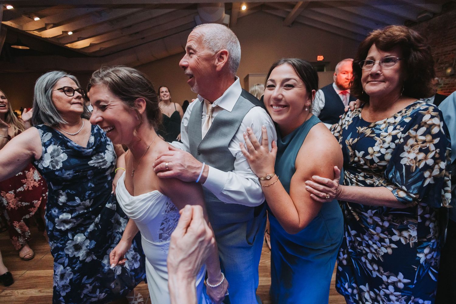Joyful wedding guests dancing together in a line at a reception, wearing elegant blue and white formal attire.