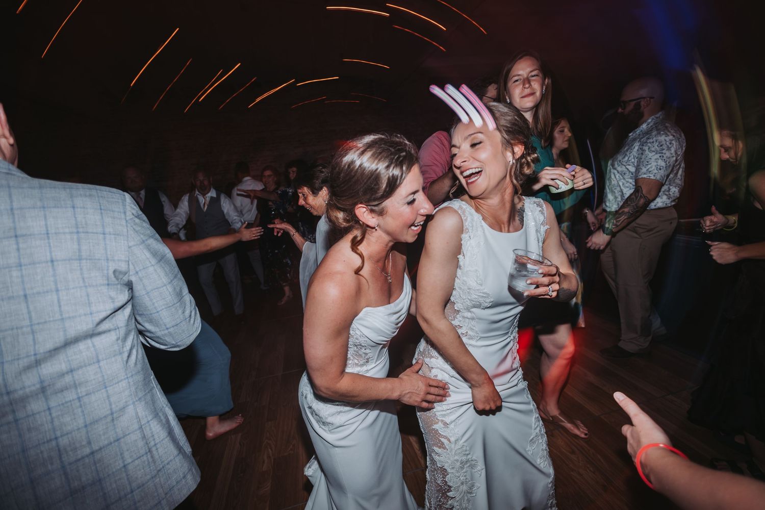 Two brides in white dresses dancing joyfully together at a wedding reception party.