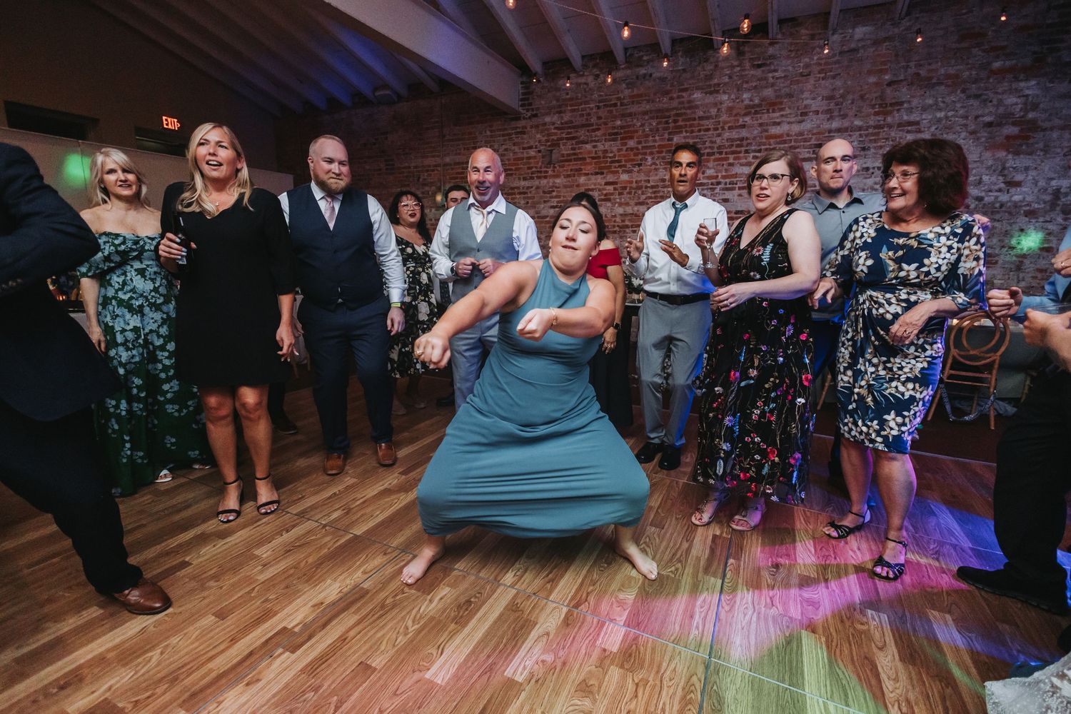 Wedding guest in teal dress doing the worm on the dance floor at a lively reception.
