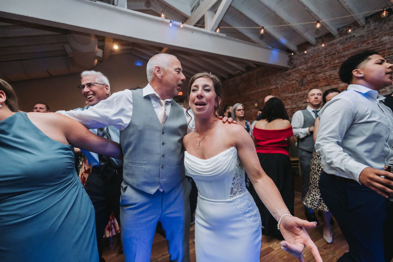 Bride and groom singing and dancing joyfully with guests at their wedding reception celebration.