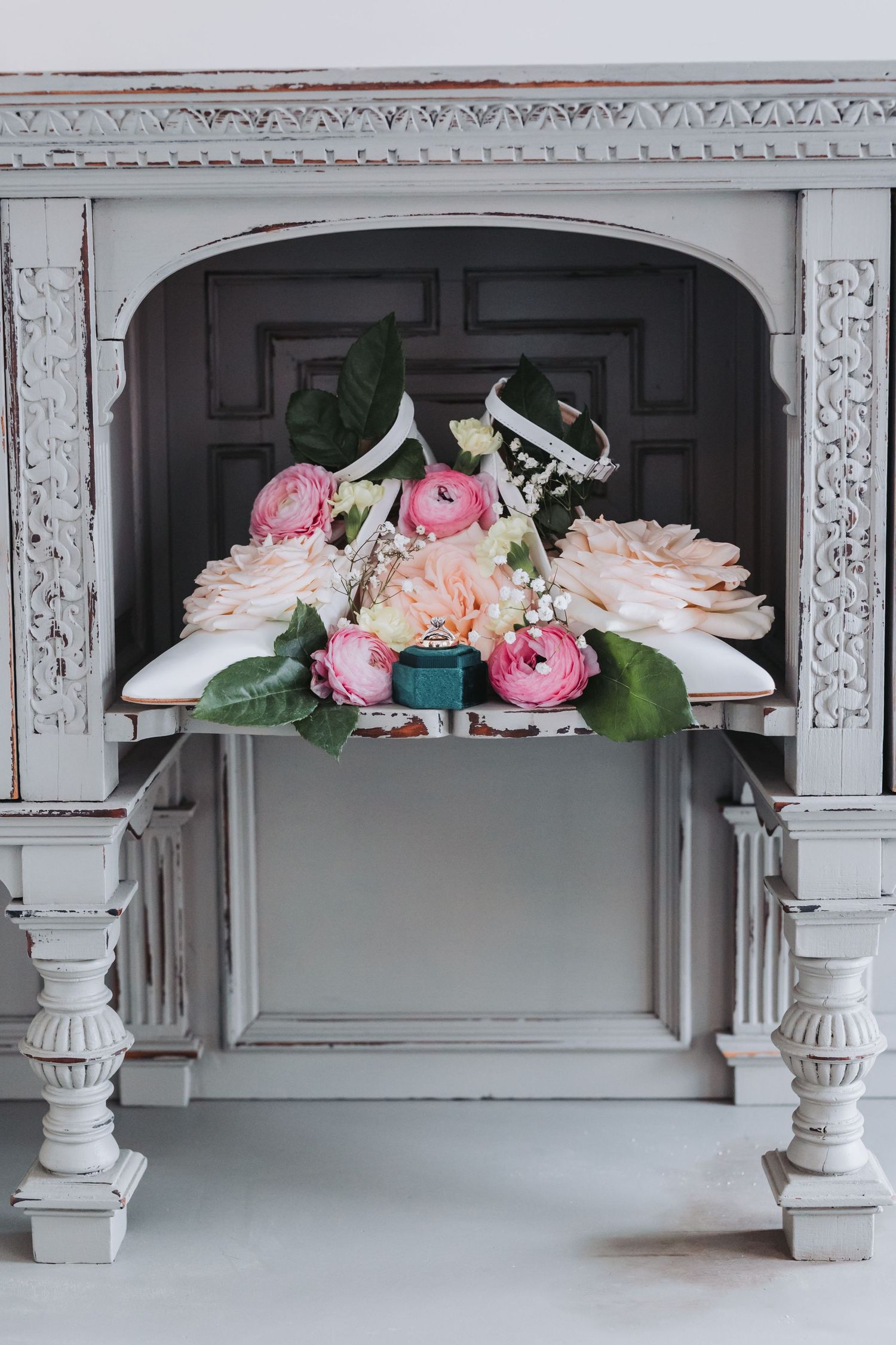 Pink and peach floral bouquet with wedding rings displayed on ornate white vintage fireplace mantel.