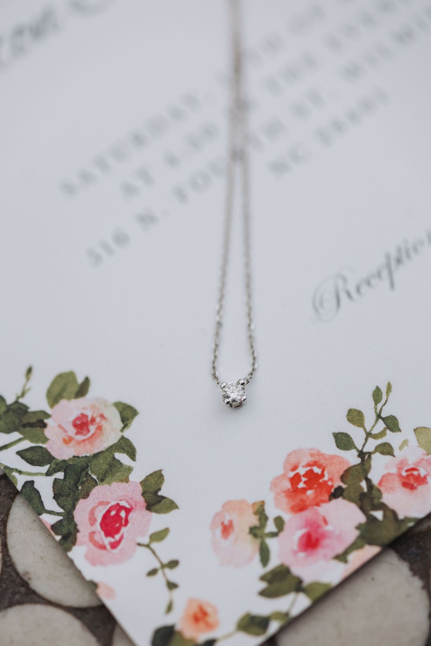 Delicate silver diamond pendant necklace resting on floral wedding invitation cards.