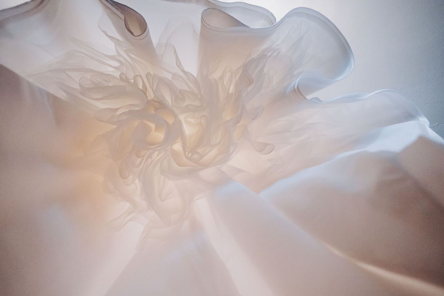 Close-up of delicate white fabric with soft ruffles and flowing texture, creating an ethereal floral appearance.