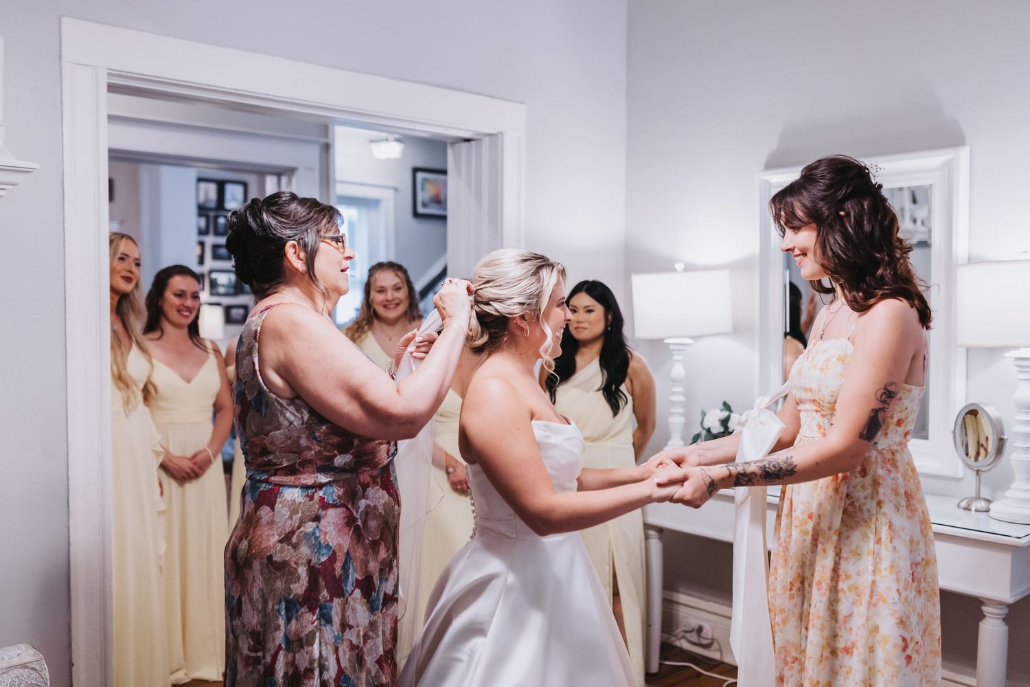 Bride laughing with bridesmaids while getting ready in bright white dressing room.