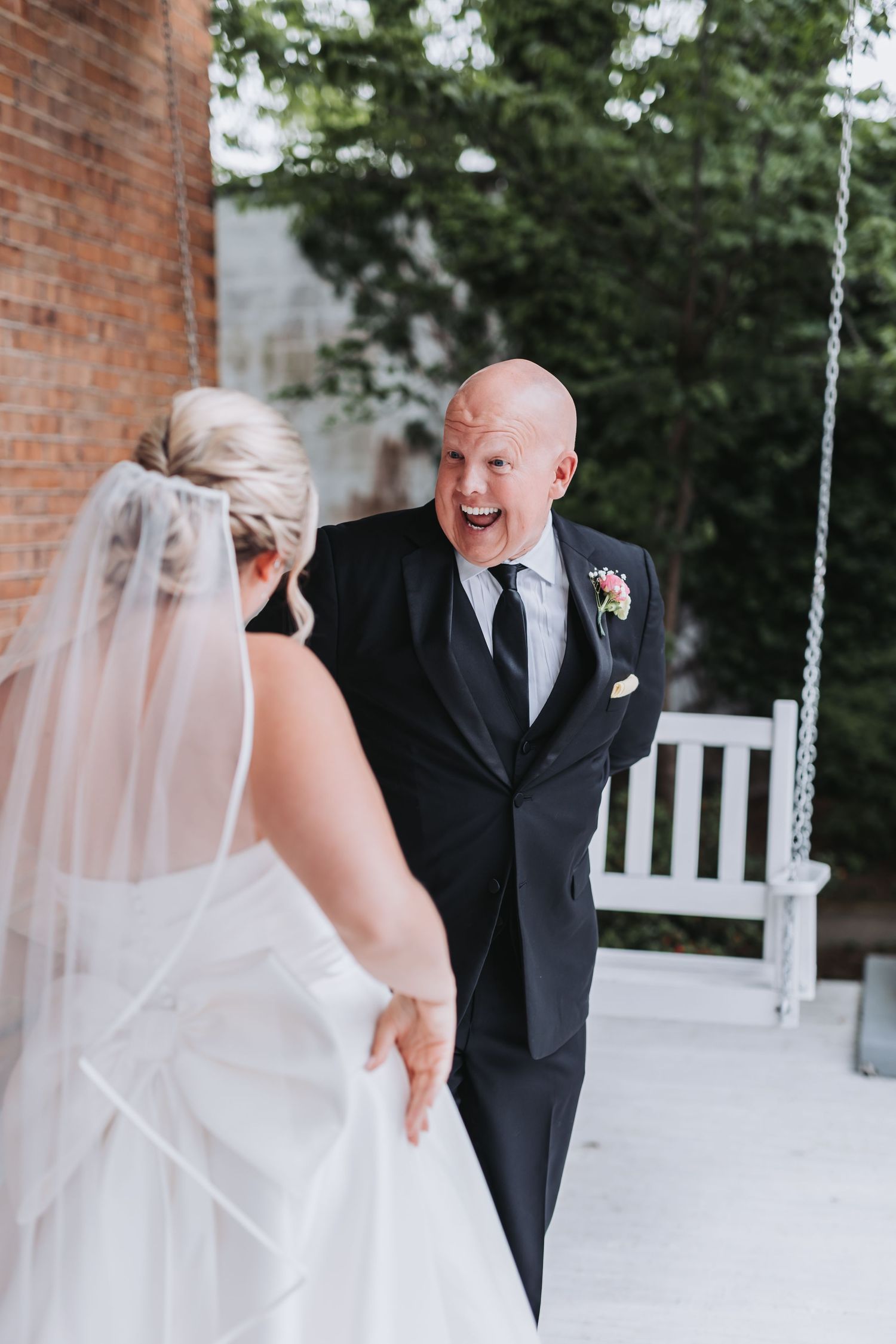 Groom in black tuxedo reacting with joy during first look with bride outdoors.