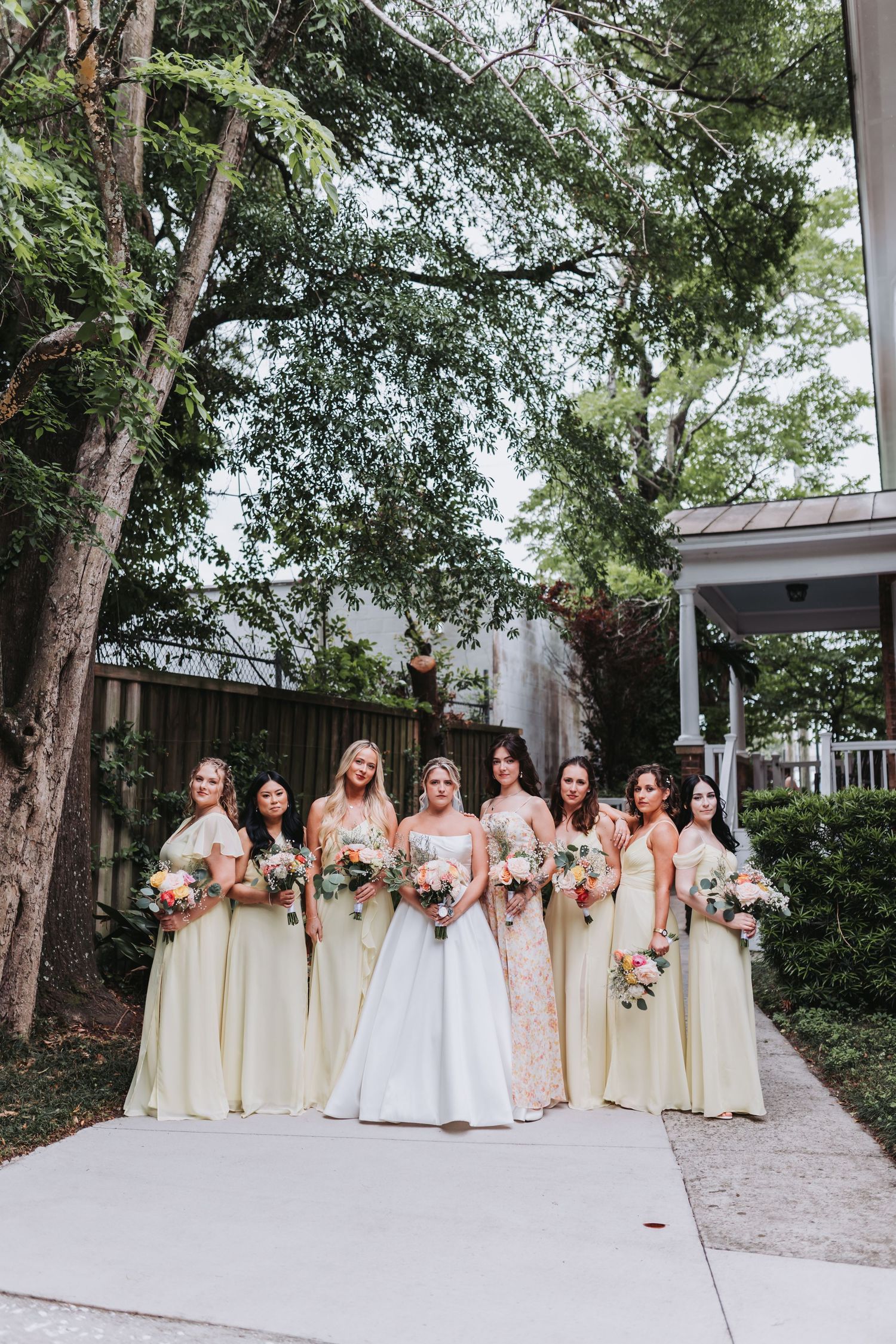 Bride in white ballgown poses with seven bridesmaids in pale yellow dresses holding colorful bouquets.