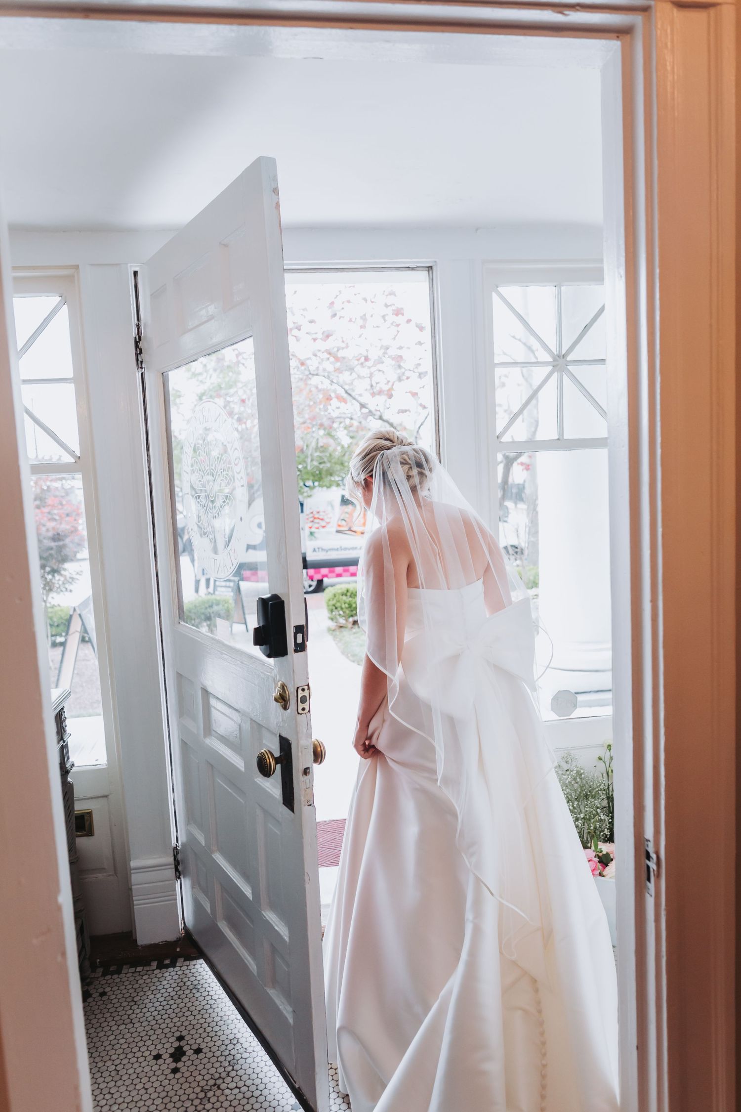 Bride in white gown and veil standing at open front door on her wedding day.