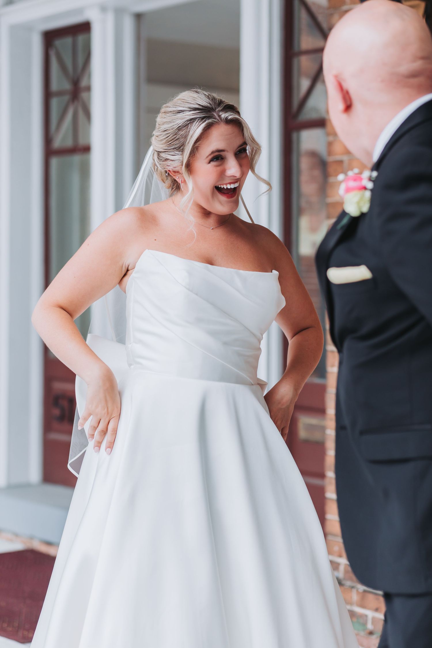 Bride in strapless white gown laughing joyfully during first look with groom in dark suit.