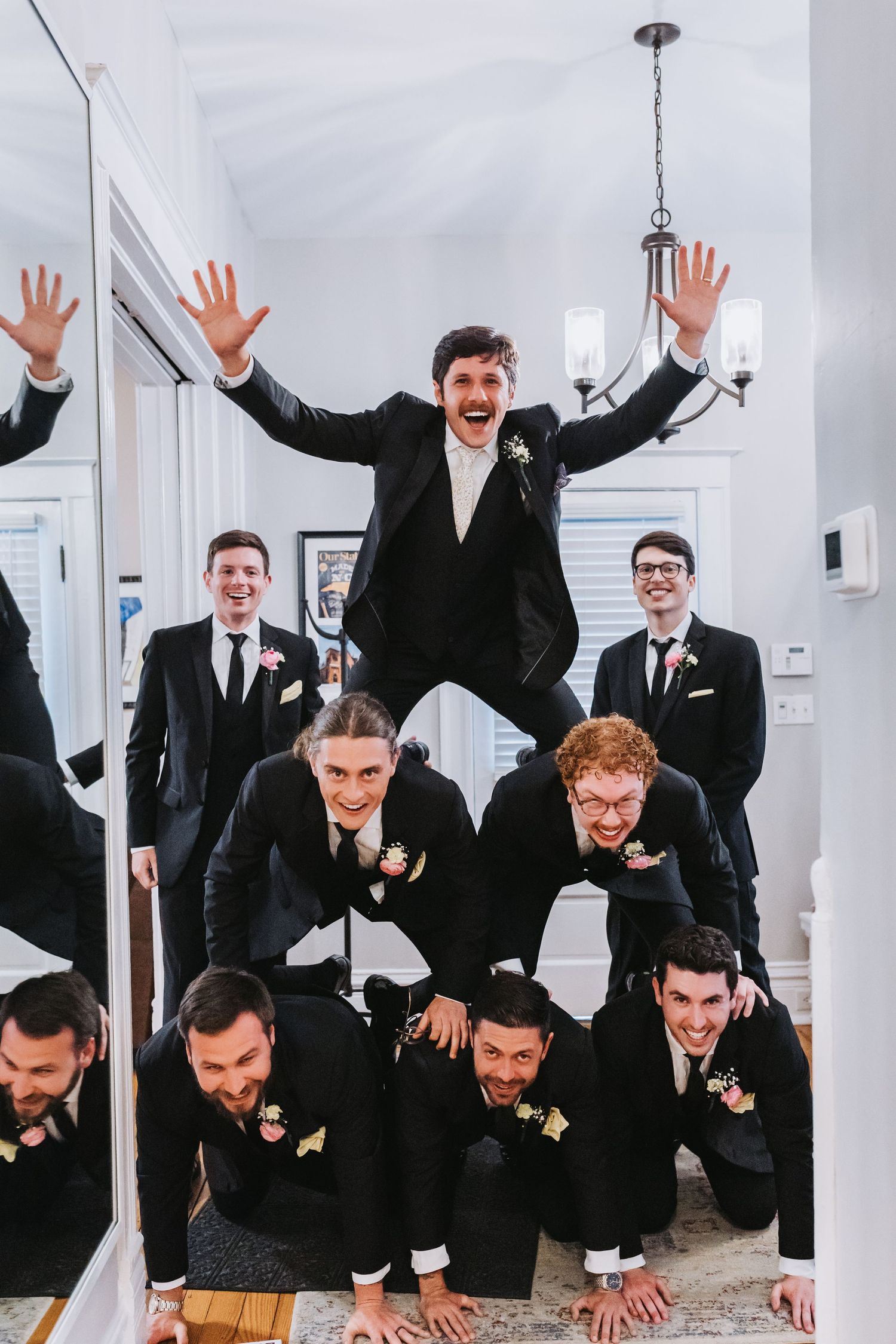 Groomsmen in black suits forming a human pyramid while celebrating before a wedding ceremony.
