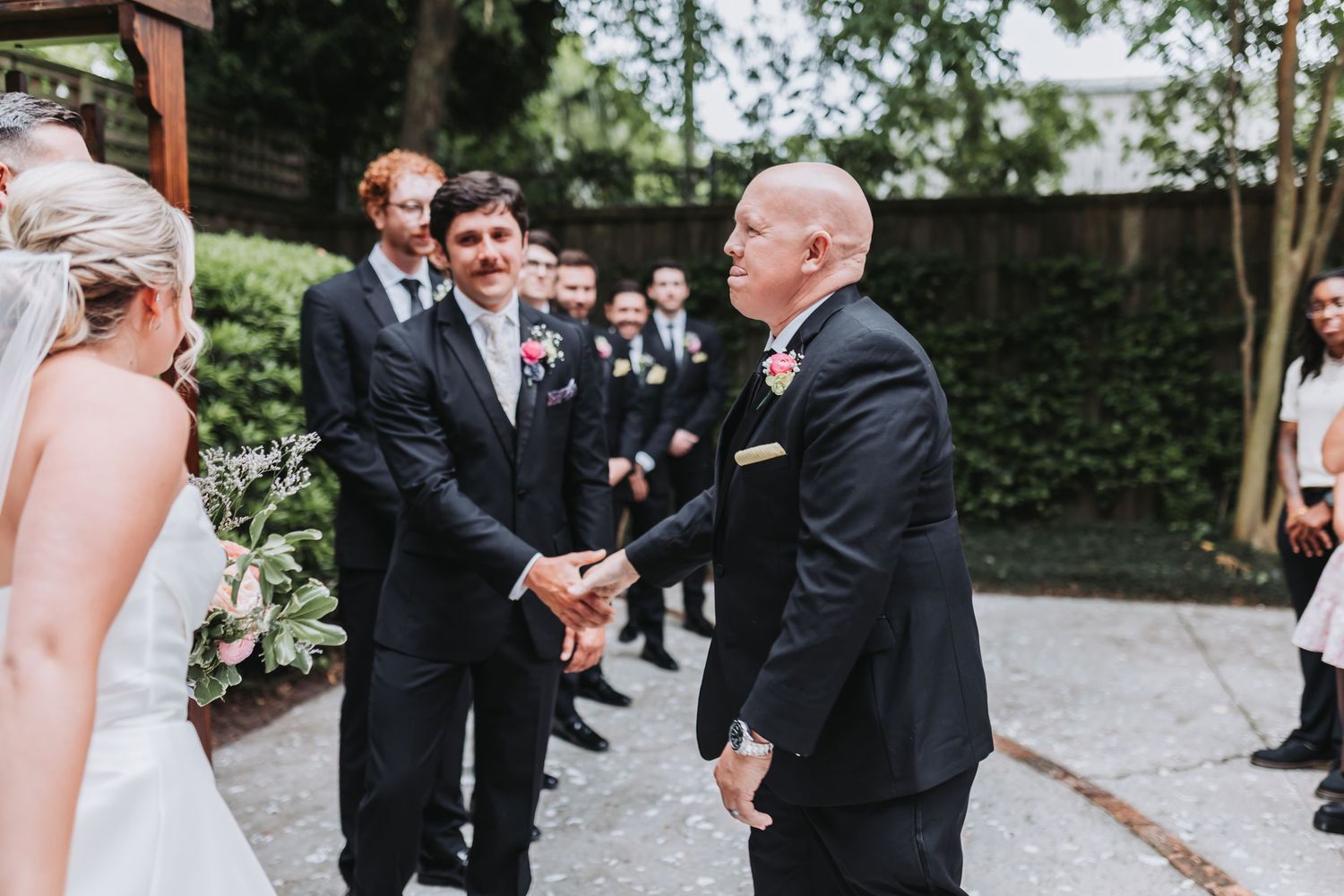 Groom shakes hands with father of the bride during outdoor wedding ceremony.