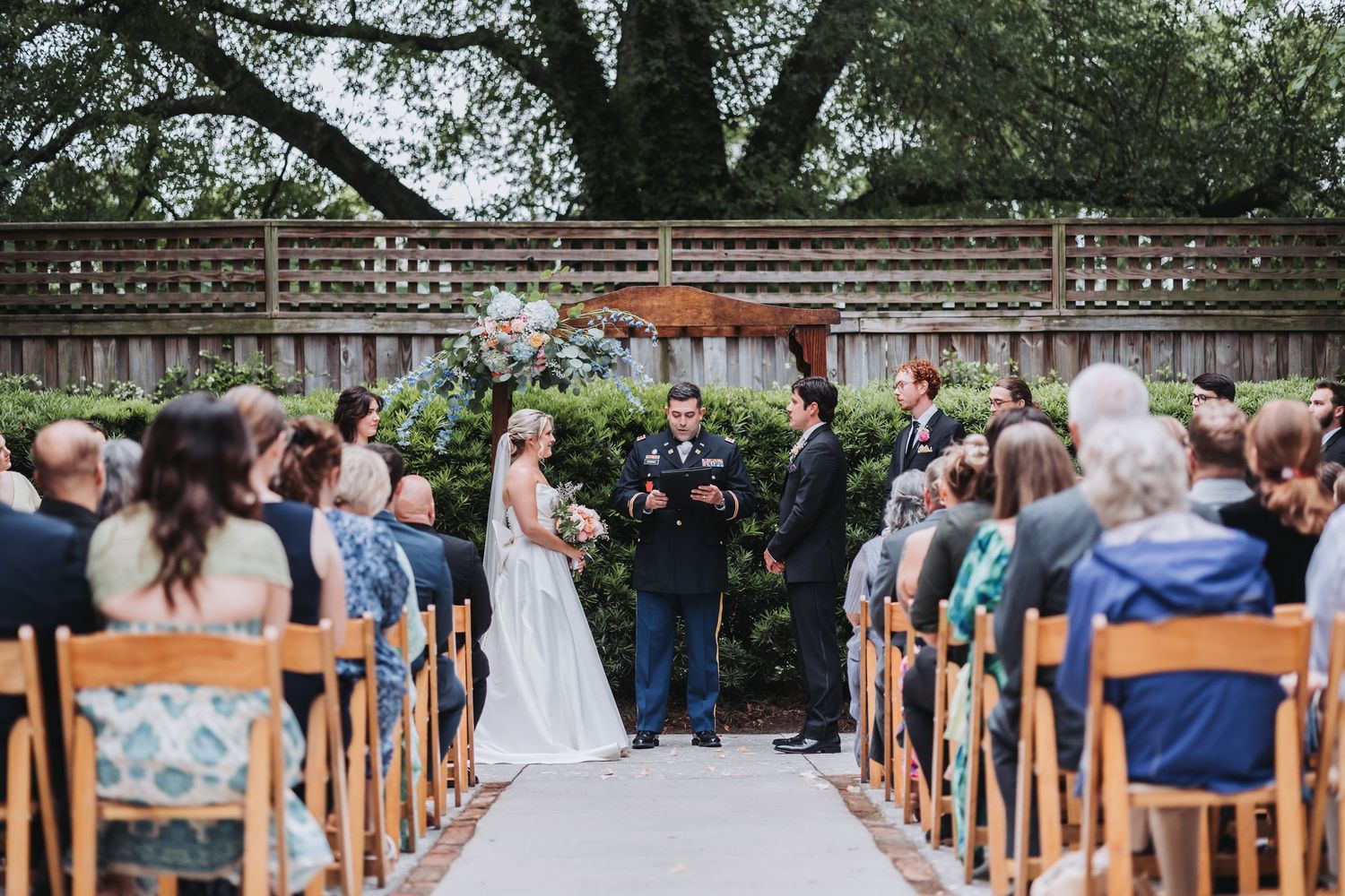 Bride and groom exchange vows at outdoor garden wedding ceremony with seated guests.