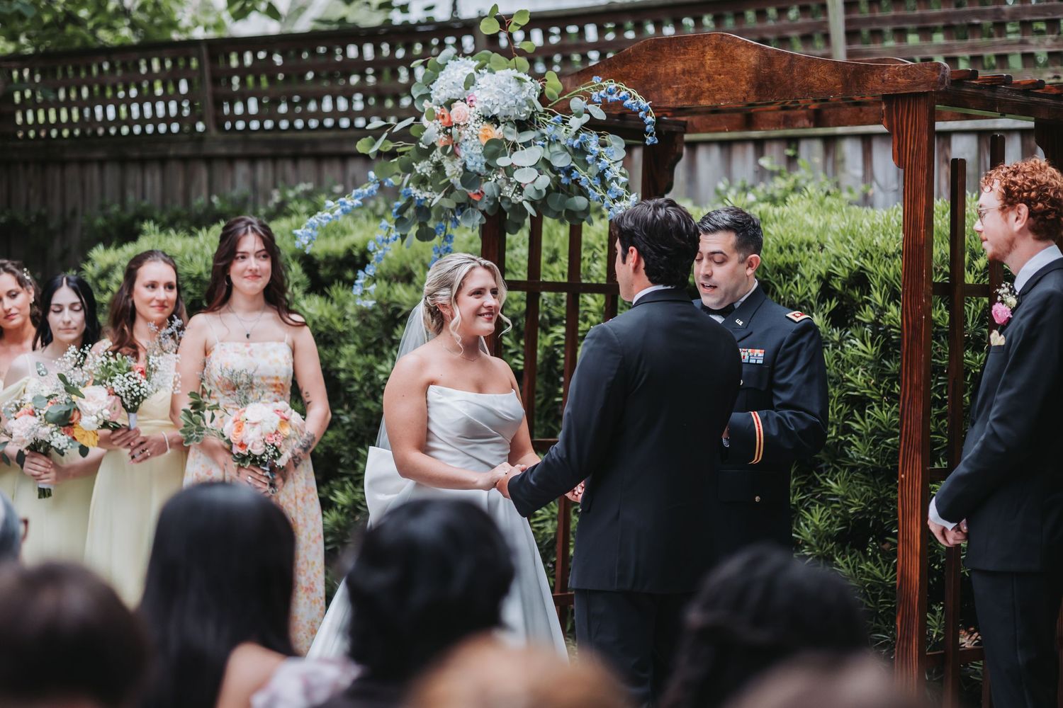 Bride and groom hold hands at outdoor garden wedding ceremony with wedding party.