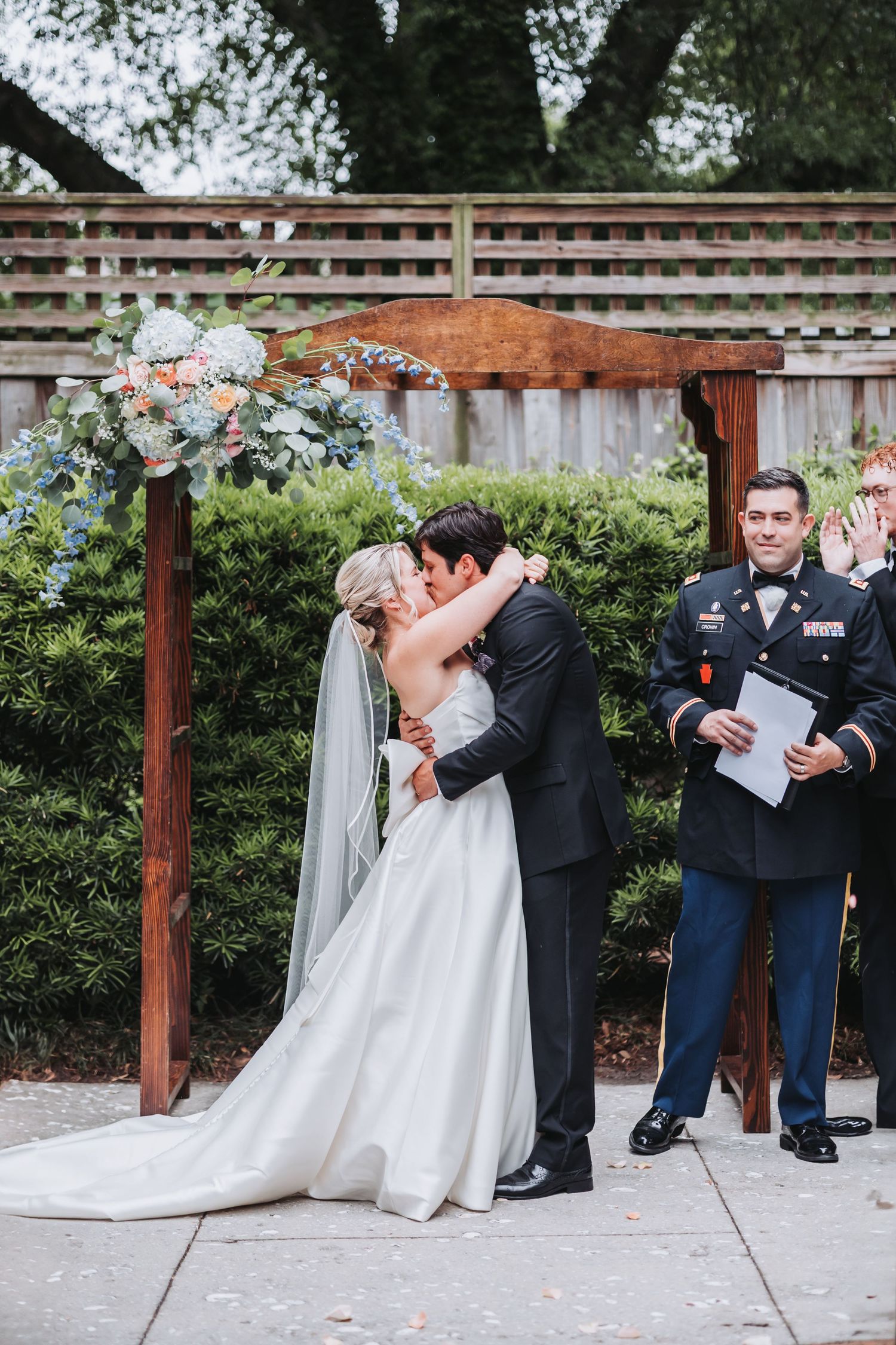 Bride and groom share their first kiss at the altar beneath a floral arch at an outdoor wedding ceremony.