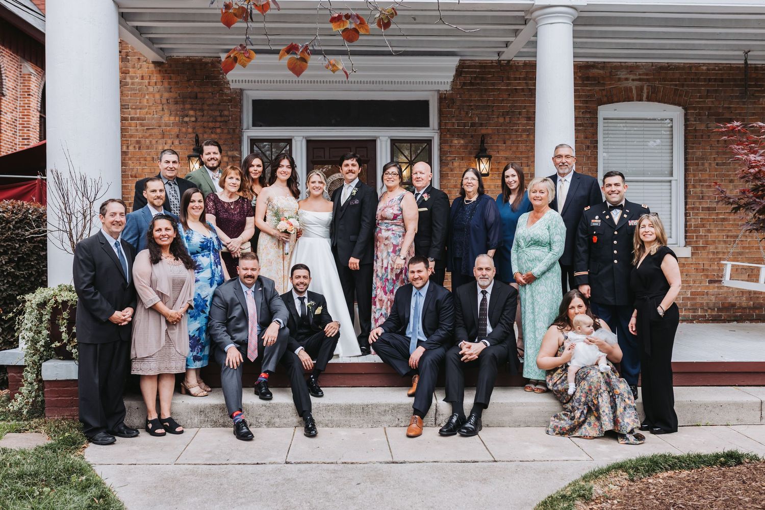 Large wedding party and family group portrait posed on the steps of a charming brick home.