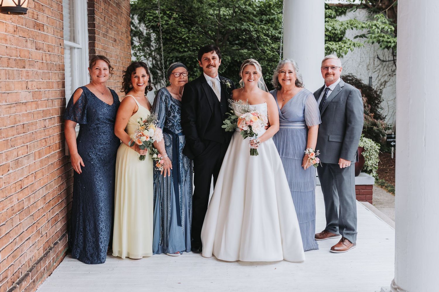 Wedding party poses together, bridesmaids in blue gowns flanking bride in white ball gown and groom in black suit.
