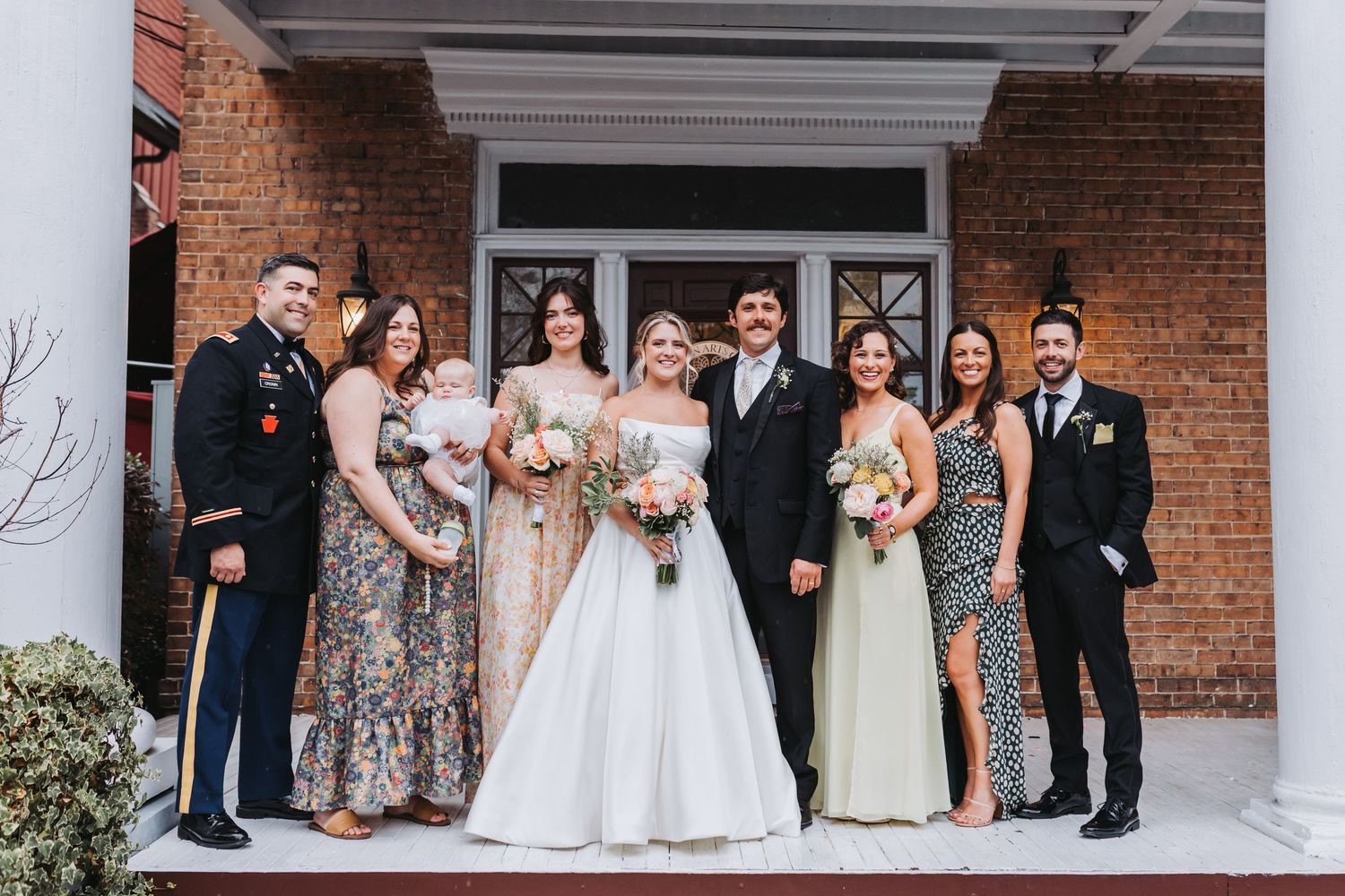 Wedding party of eight posing on brick building steps with bride in white gown and groom.