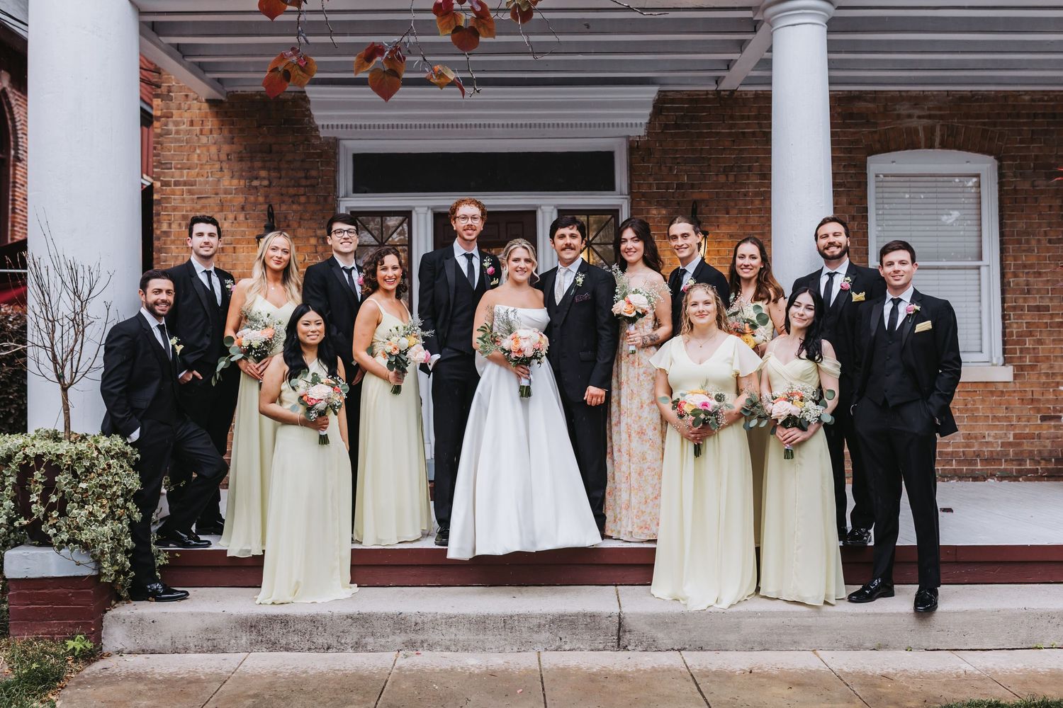 Large wedding party posing on steps in black suits and light green bridesmaid dresses with bride.