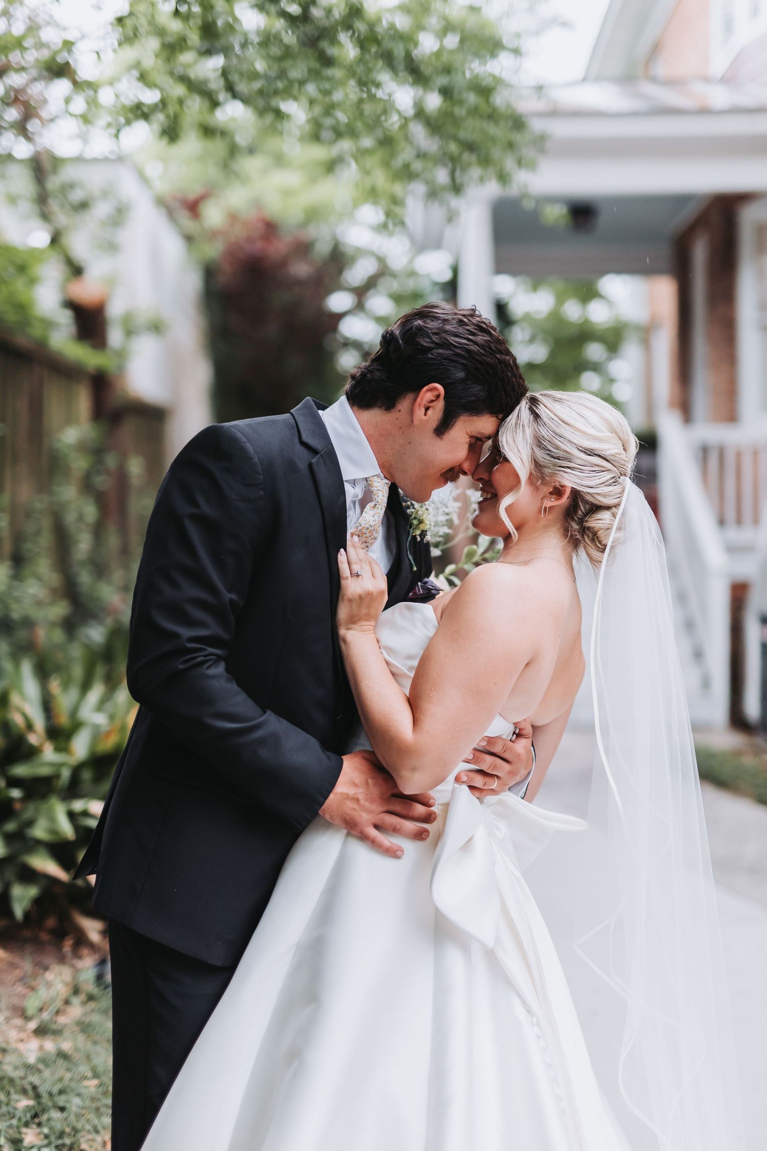 Bride and groom sharing a romantic forehead touch in a garden on their wedding day.