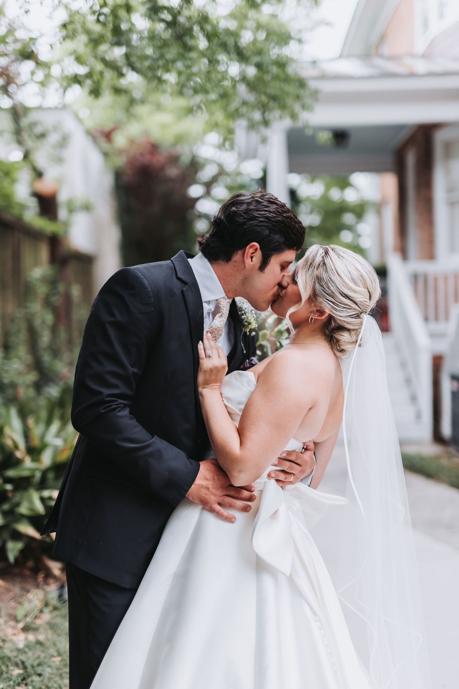 Bride and groom share a romantic kiss outdoors, bride in elegant white ballgown with veil.
