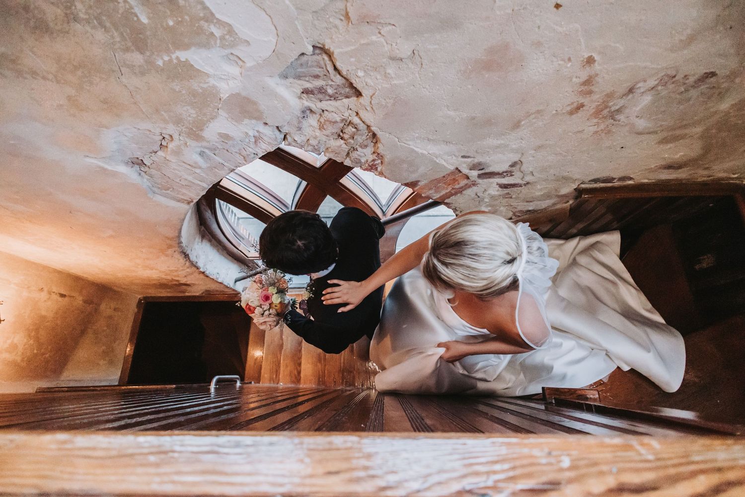 Aerial view of bride and groom walking up wooden stairs in a rustic venue.