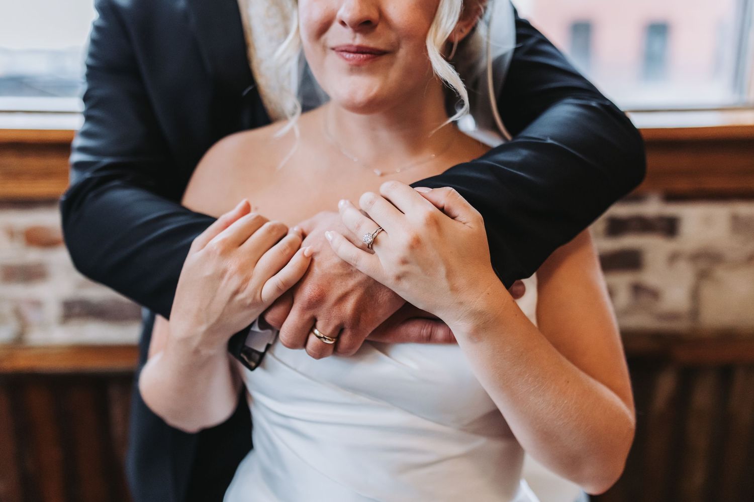 A close-up of a bride and groom showing off their wedding rings, her hands resting gently on his arm.