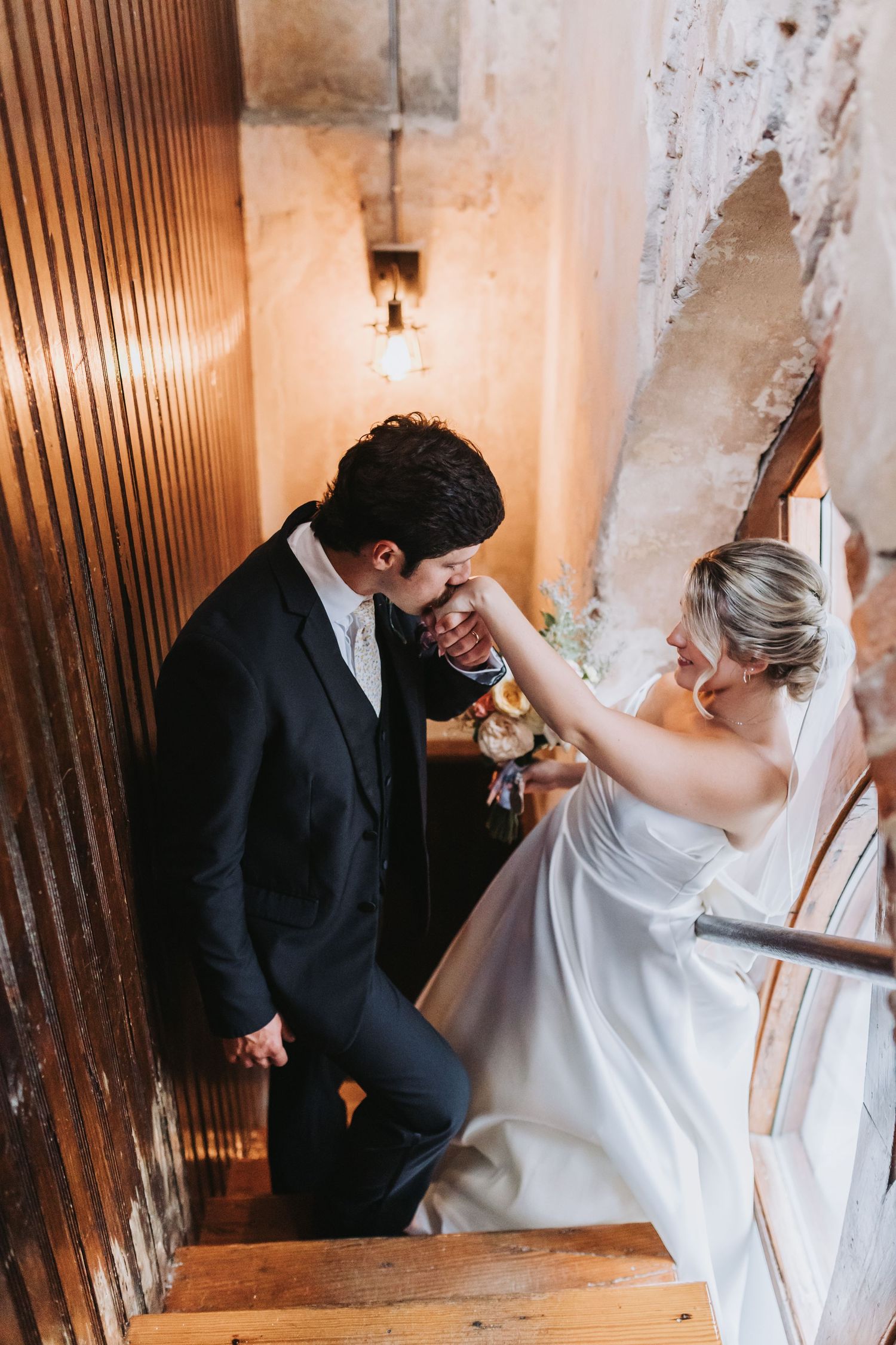 Bride playfully touches grooms face as they share a romantic moment on wooden staircase.