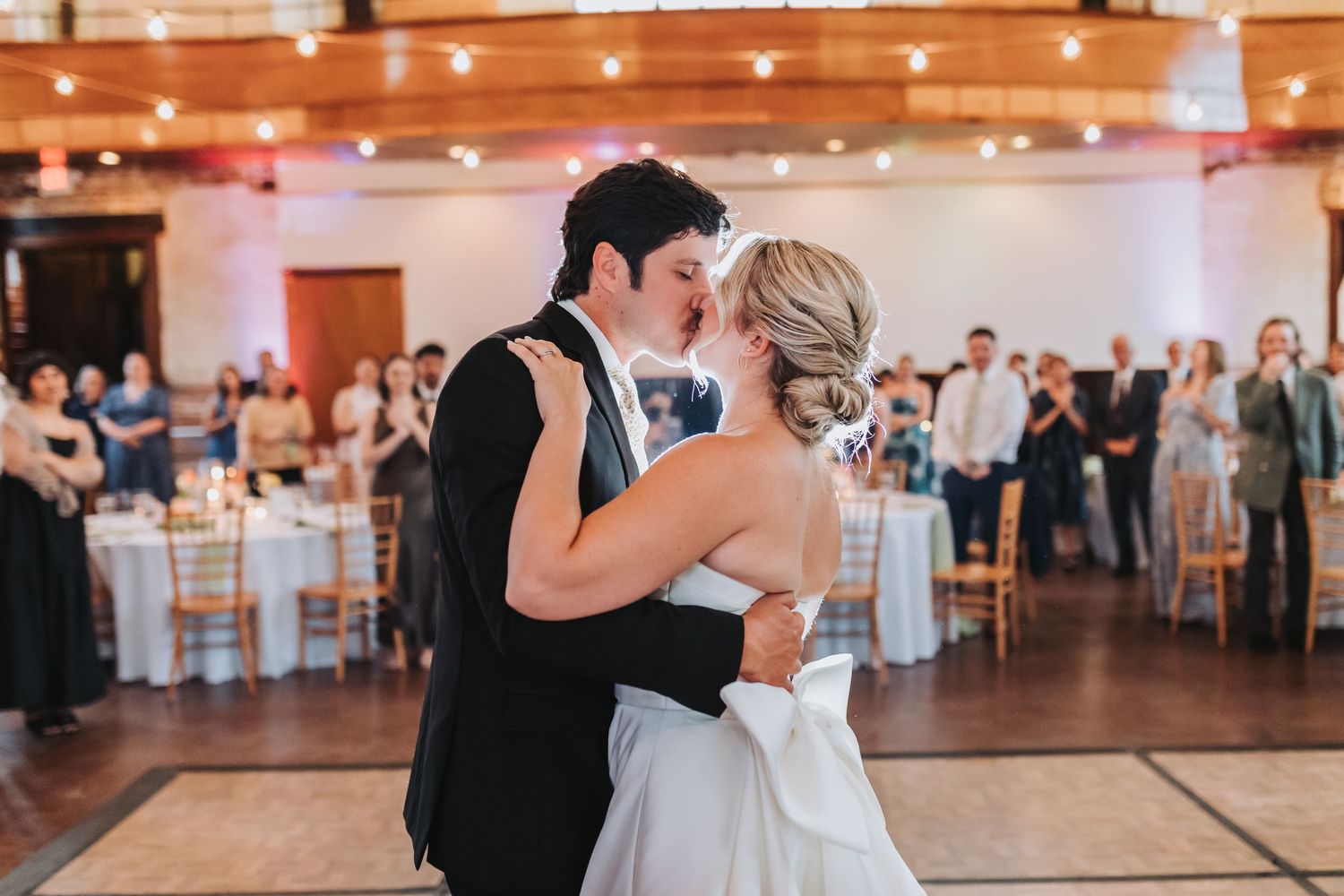 Bride and groom share first dance kiss on dance floor at wedding reception.