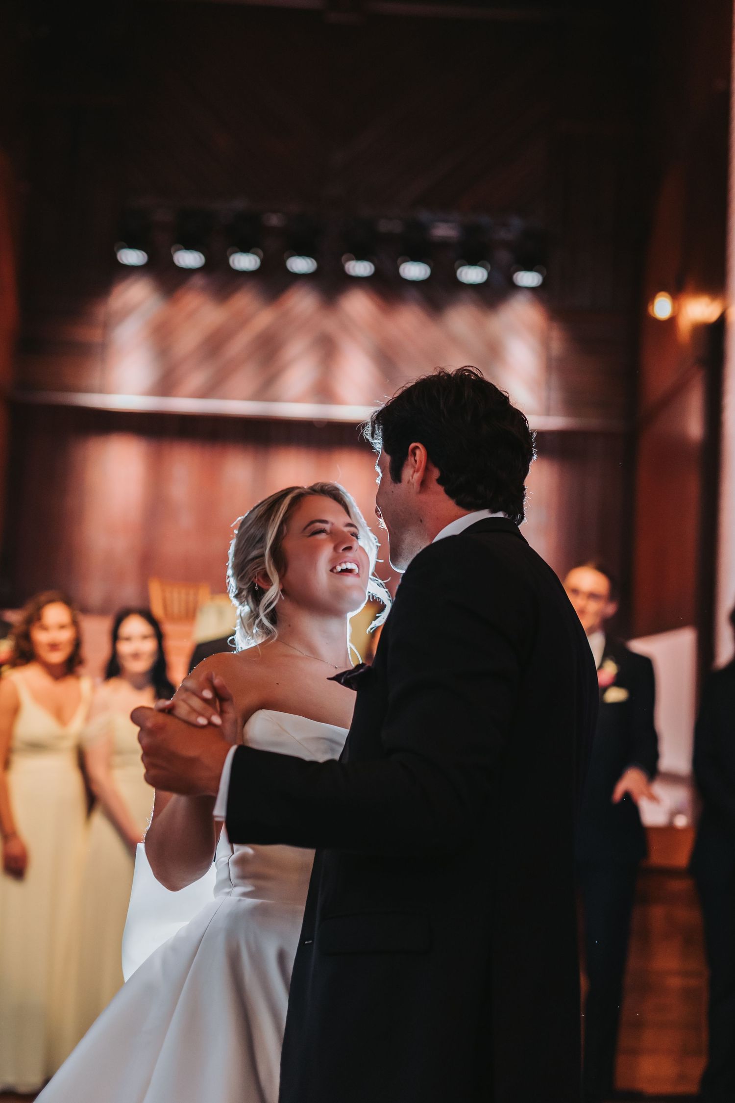 Bride and groom share a joyful first dance at their wedding reception in a warmly lit venue.