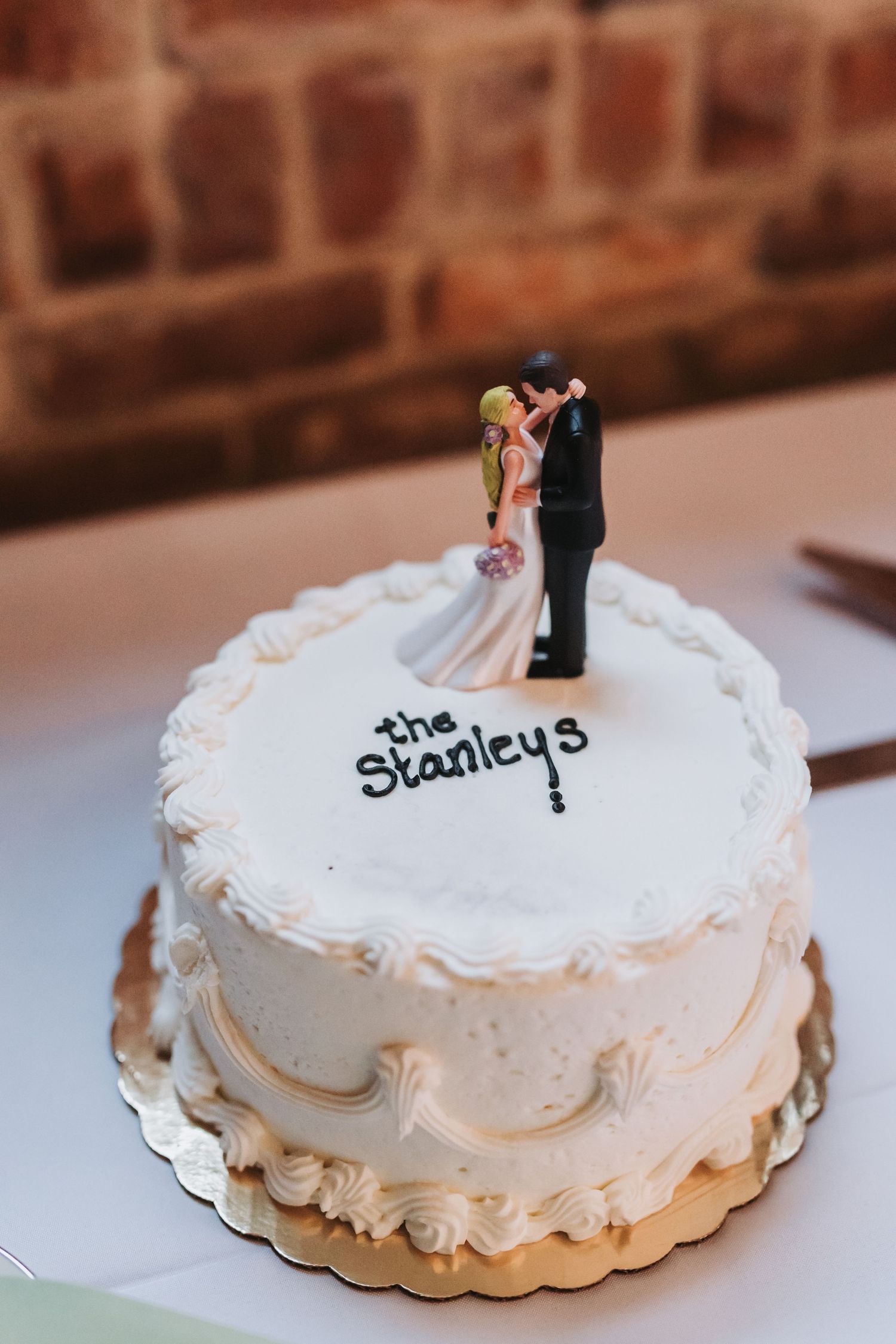 White wedding cake with bride and groom topper reading the Stanleys in elegant script frosting decoration.