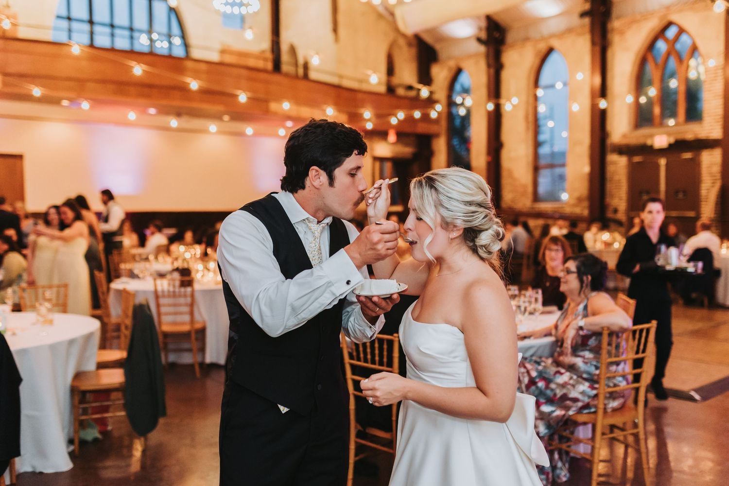 Bride and groom share a champagne toast during their elegant wedding reception in a warmly lit historic venue.