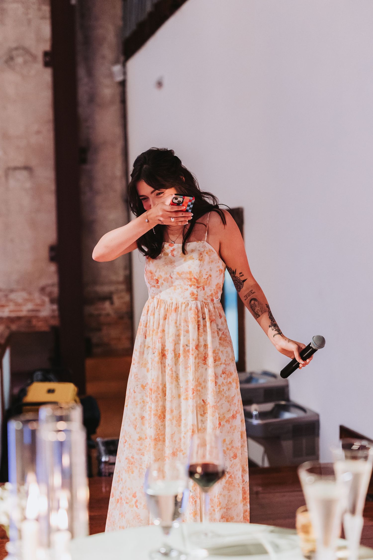 Emotional bridesmaid wipes tears while giving a heartfelt wedding speech holding a microphone.