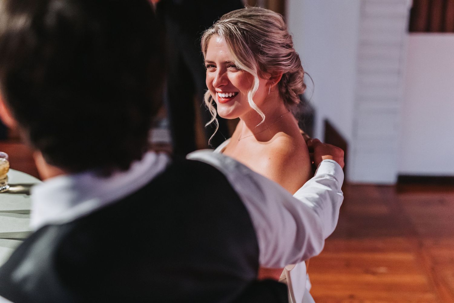 A smiling blonde bride in a white off-shoulder gown glows during her wedding reception.