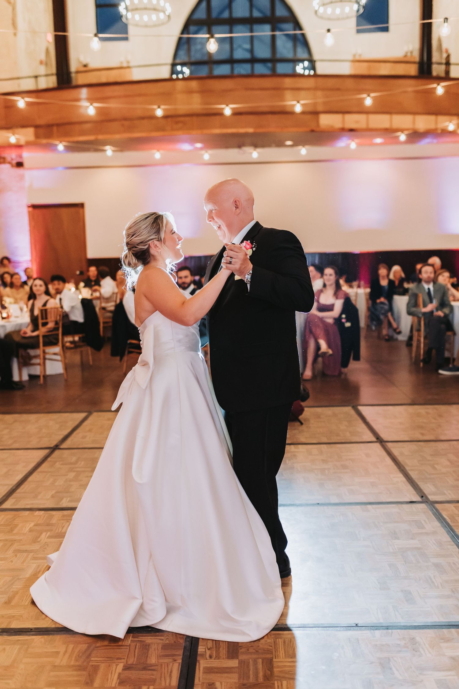Bride in white gown shares emotional father-daughter dance in elegant ballroom reception.