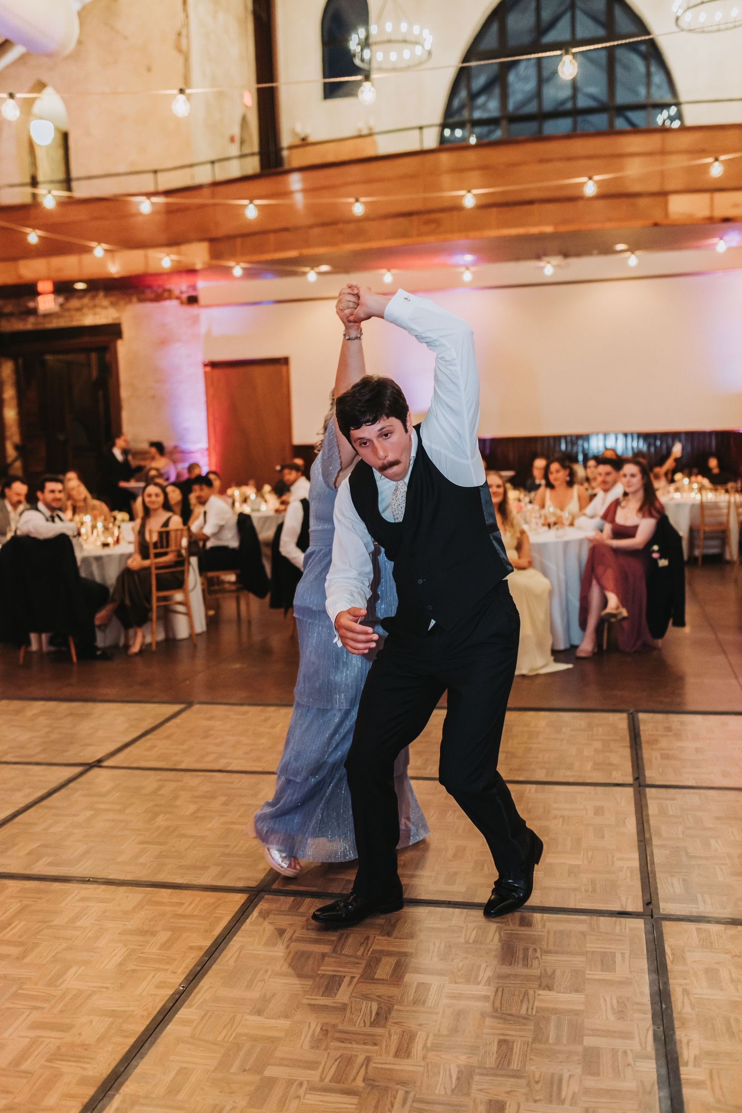 Groomsman performs energetic dance move with bridesmaid on wedding reception dance floor.