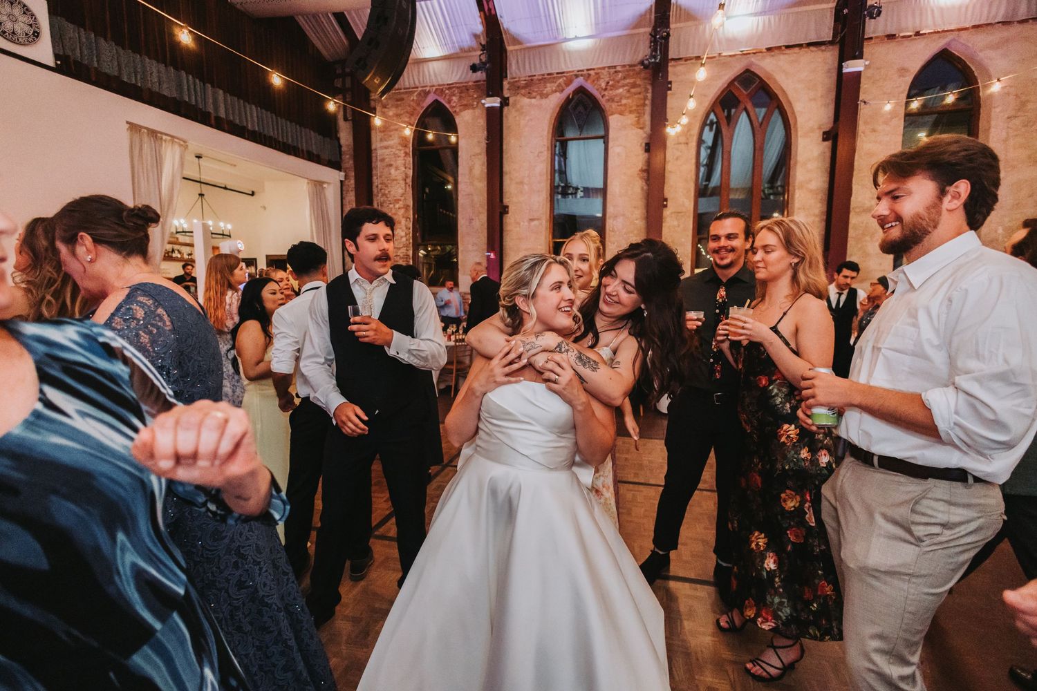 Bride in white gown dances joyfully with guests during lively wedding reception celebration.