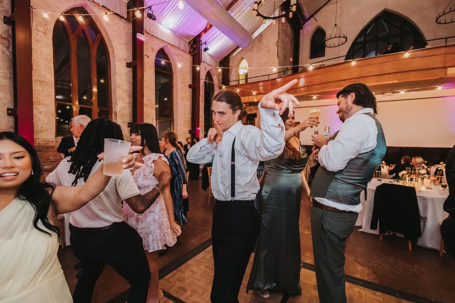 Wedding guests dance energetically on the floor of a beautifully lit reception venue.