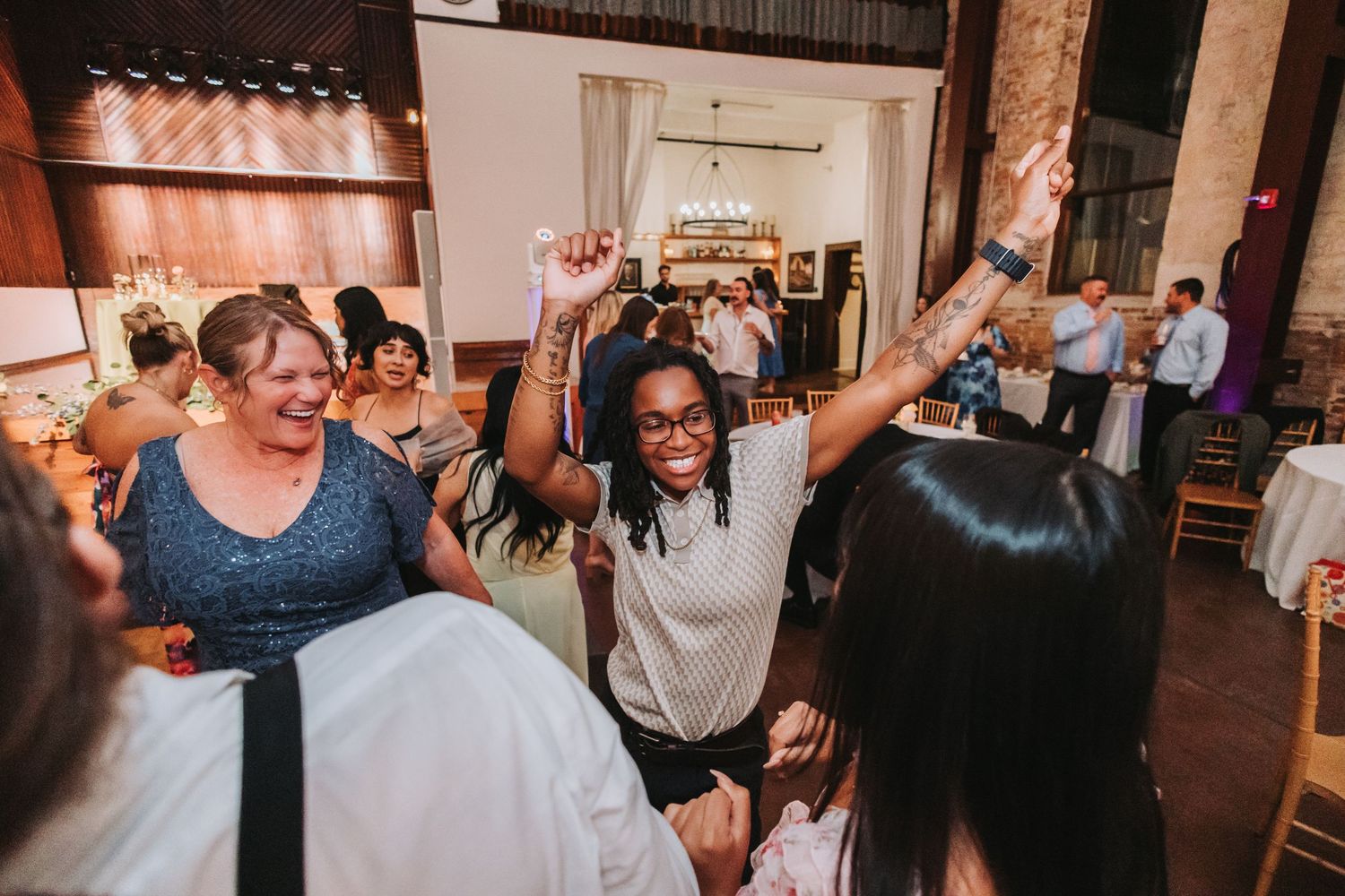 Guests celebrate with raised hands on the dance floor at a lively wedding reception.
