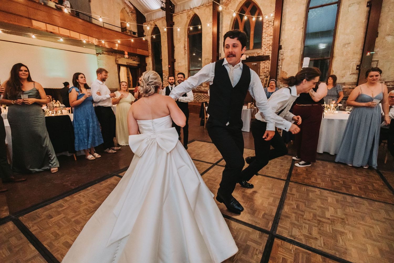 A bride and groom dance energetically on the wooden dance floor at their wedding reception.