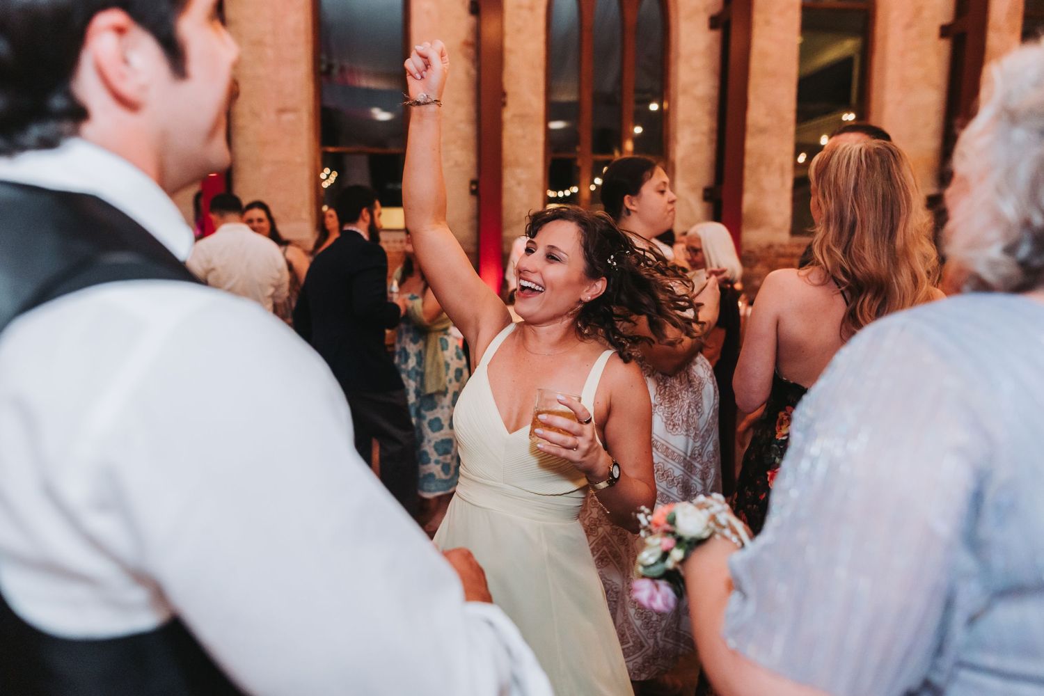 Bride in white dress dancing joyfully with raised arm at wedding reception celebration.