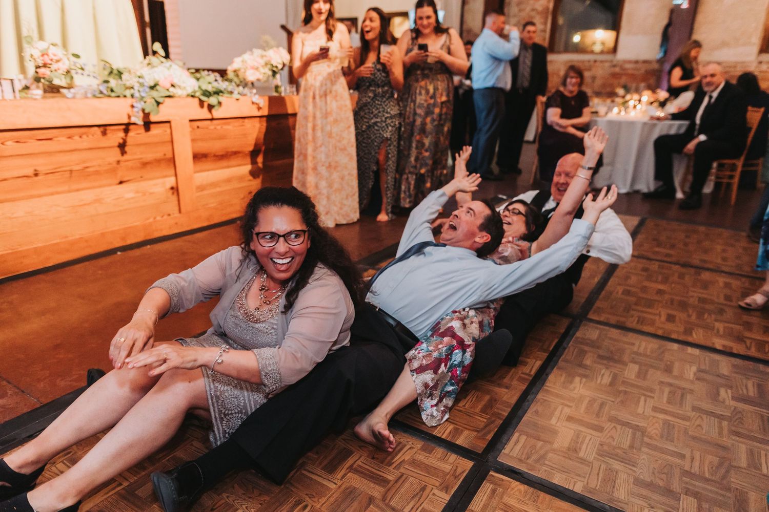 Guests laughing and sliding on dance floor during lively wedding reception celebration indoors.