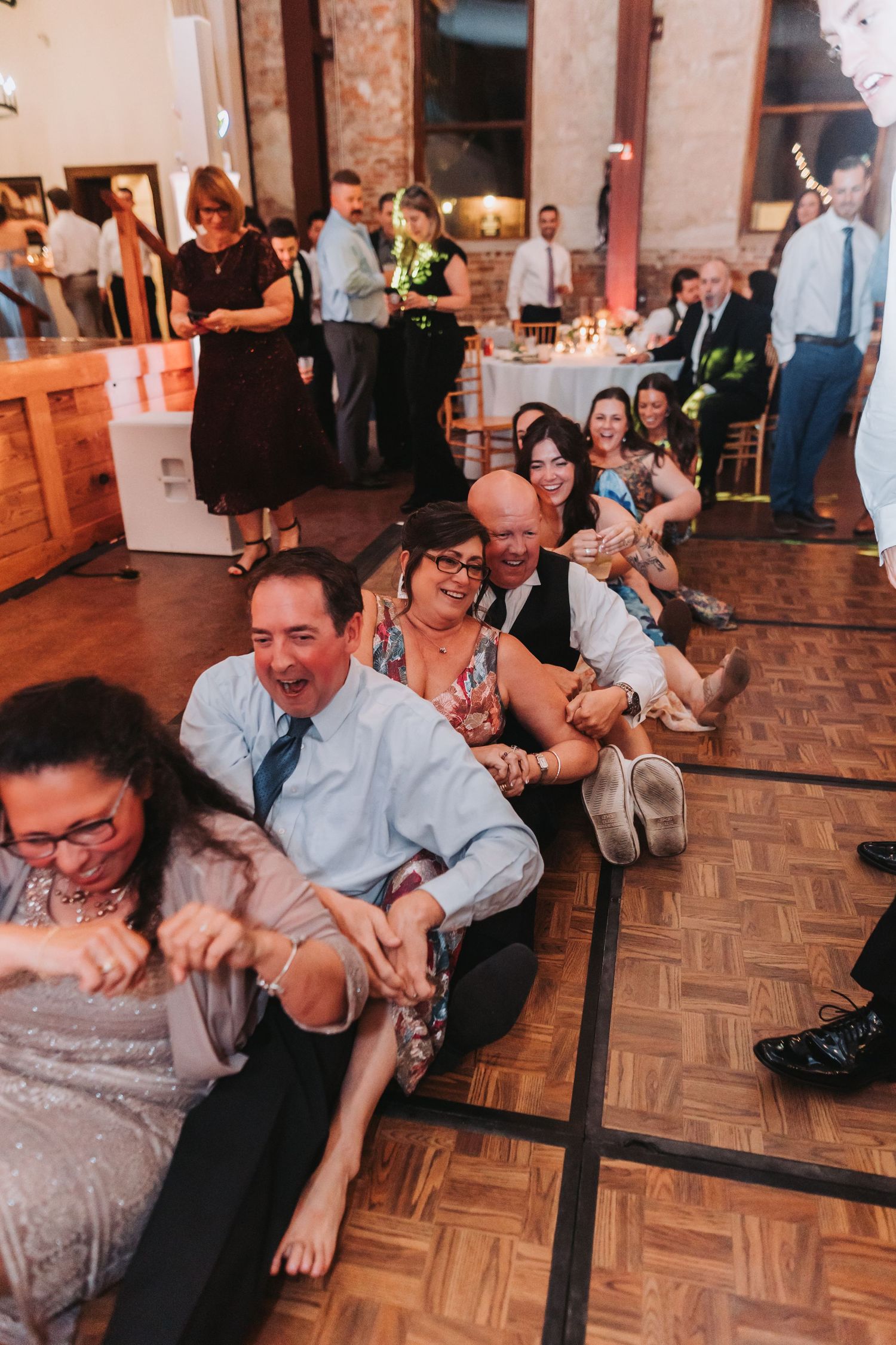 Wedding guests laughing and sitting on dance floor during fun reception activity.
