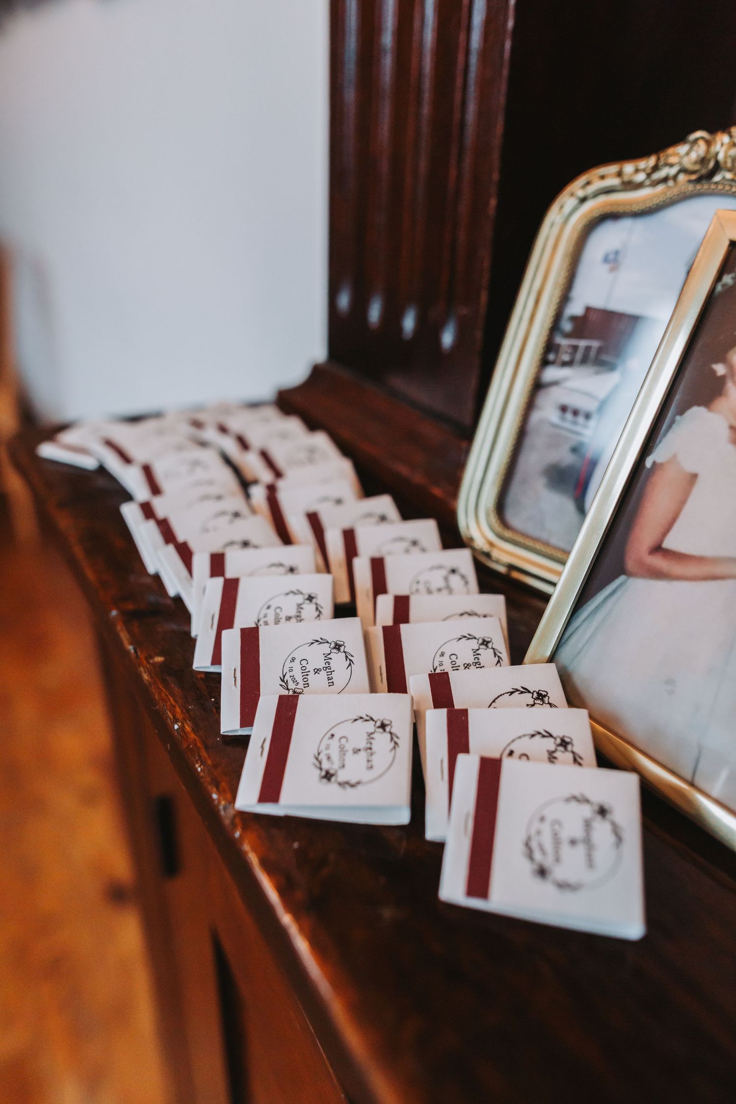 Elegant wedding matchbooks with monogram H logo lined up on antique wooden dresser beside framed bridal photo.