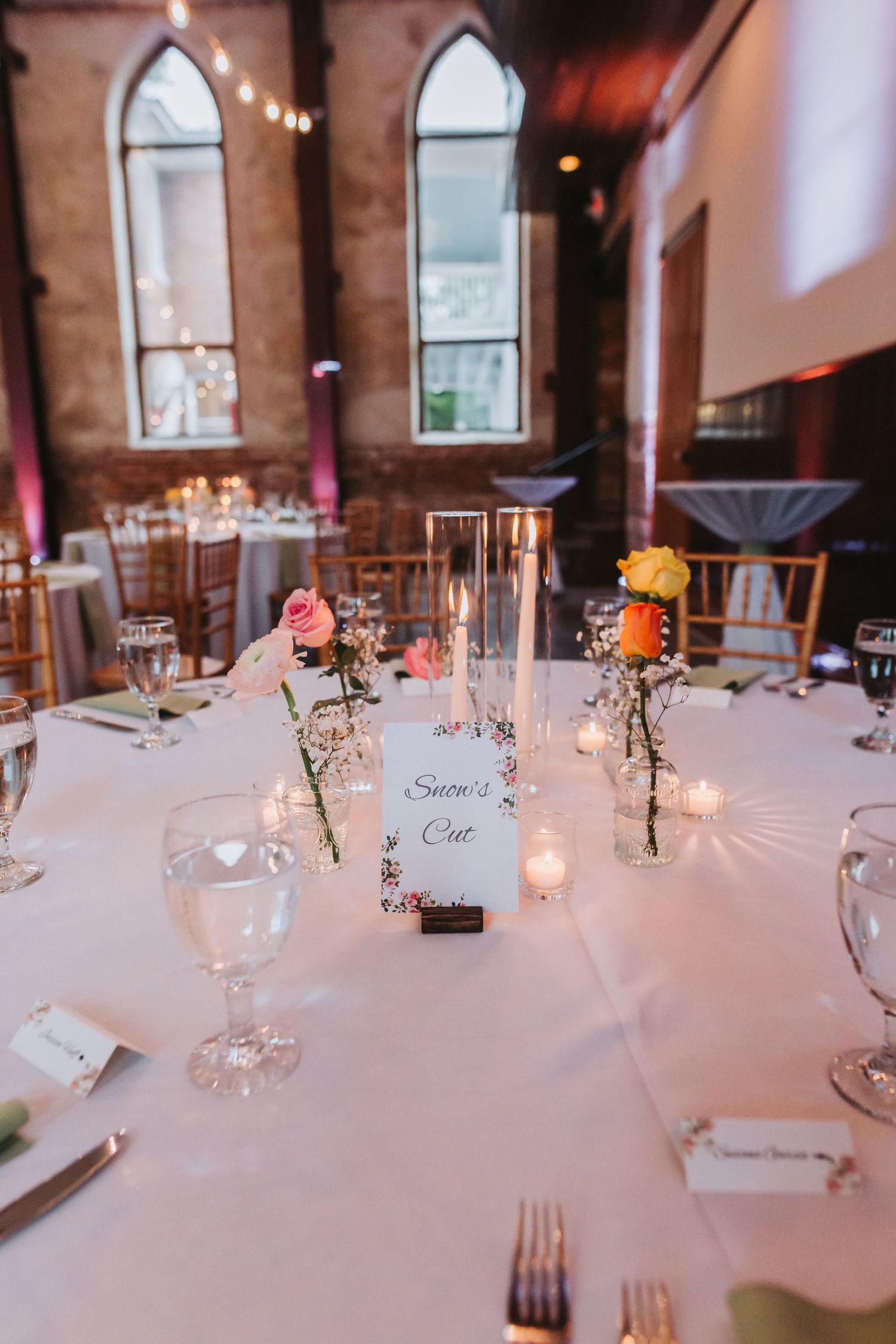Elegant wedding reception table with white linens, floral centerpieces, candles, and a Snow's Cut table name card.