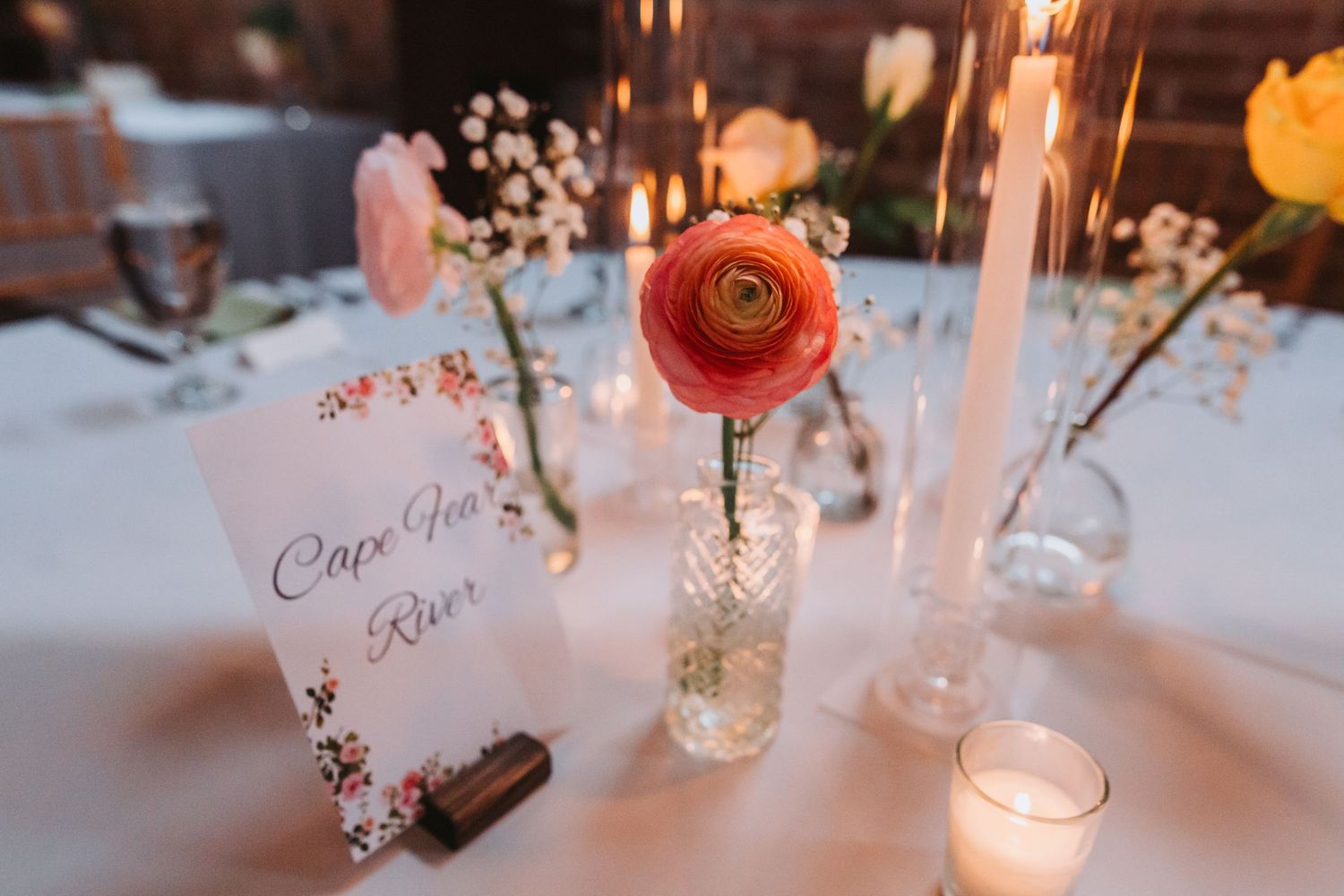 Elegant wedding table with coral ranunculus, baby's breath, candles, and a floral Cape Cod River table number card.