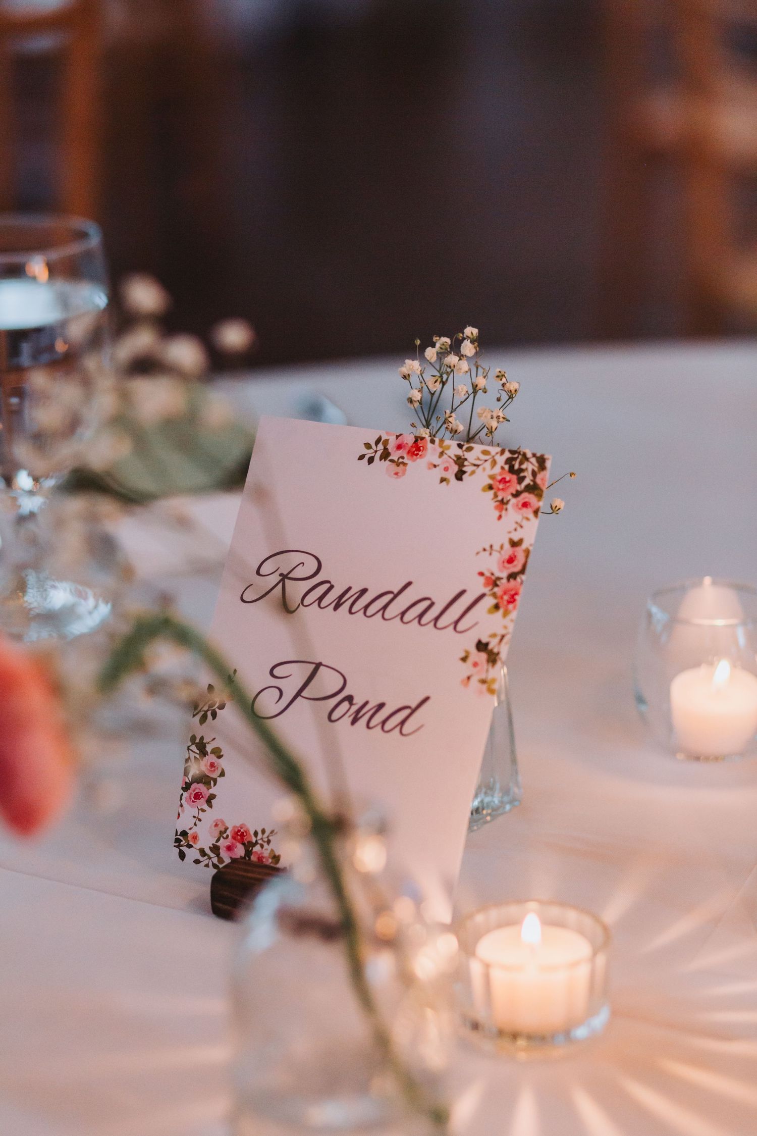 Elegant floral wedding table card reading Randall Pond surrounded by candles and flowers.