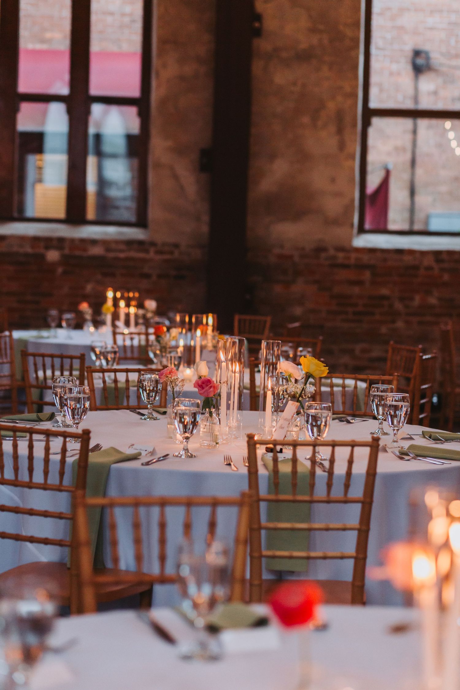 Elegant wedding reception tables with chiavari chairs, candles, and floral centerpieces in rustic brick venue.