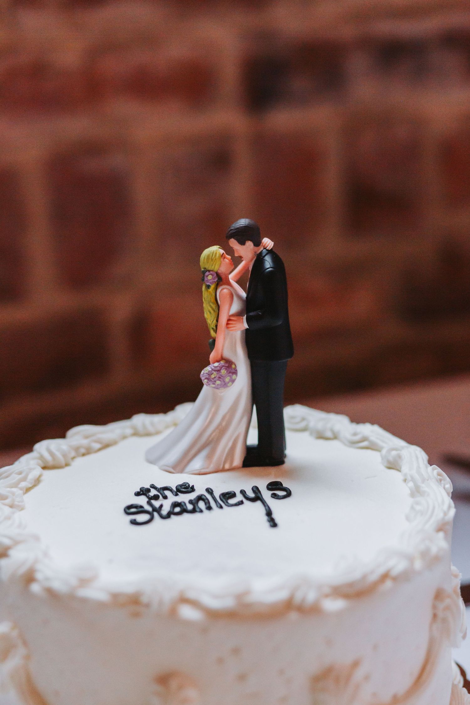 White wedding cake topped with kissing bride and groom figurines inscribed with the Stanleys on the frosting.