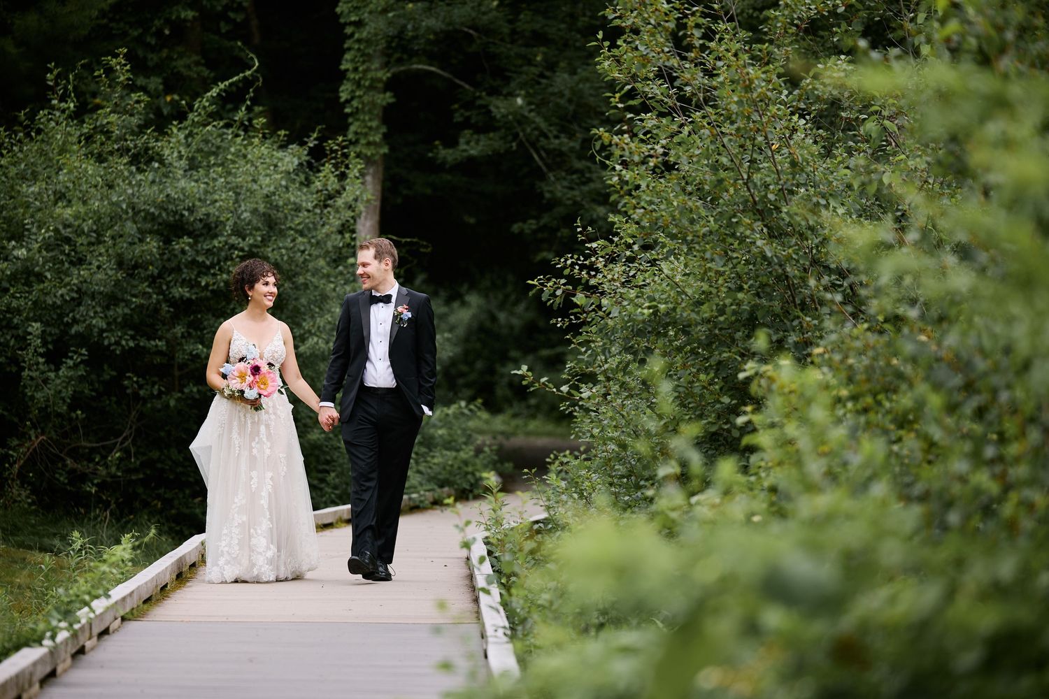 A happy couple walks along a winding path at the Willowdale Estate surrounded by lush green trees and countryside scenery.
