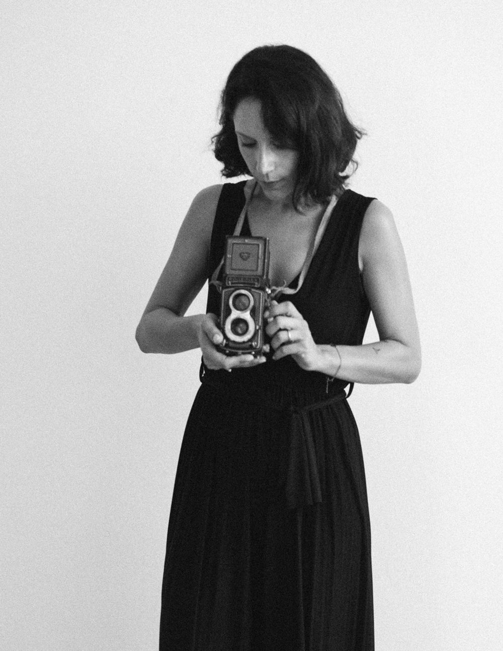 Black and white portrait of a woman in a black dress holding a vintage Rolleiflex camera.
