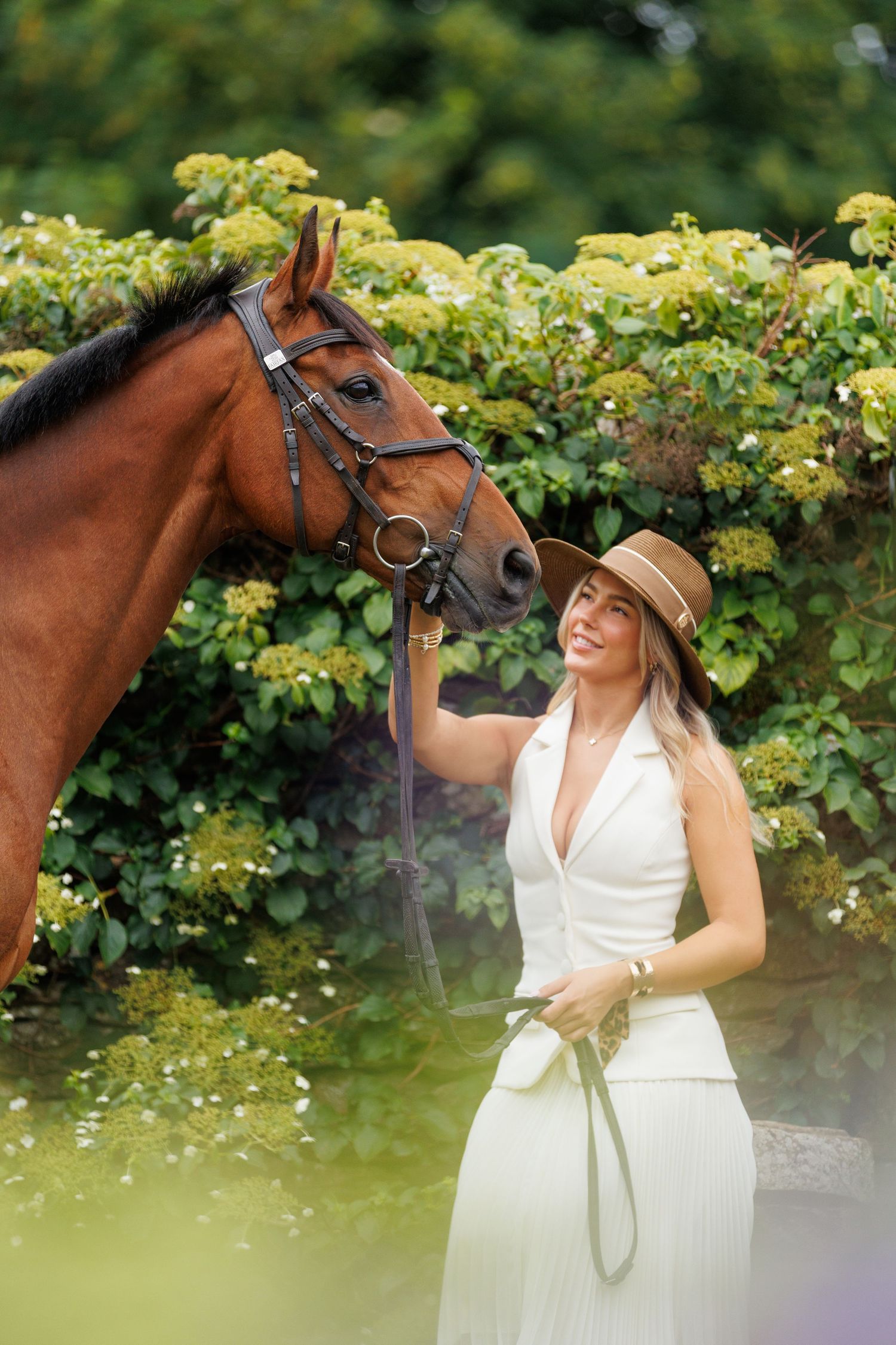 A brown horse and rider in a white sweater pose together against autumn foliage in soft natural lighting.